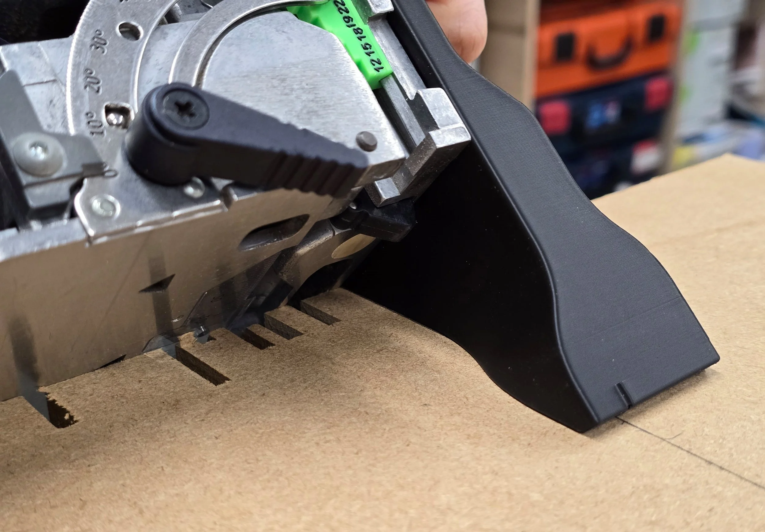 The spline jig's wide base resting against the corner edge of an MDF board with a row of spline slots already cut