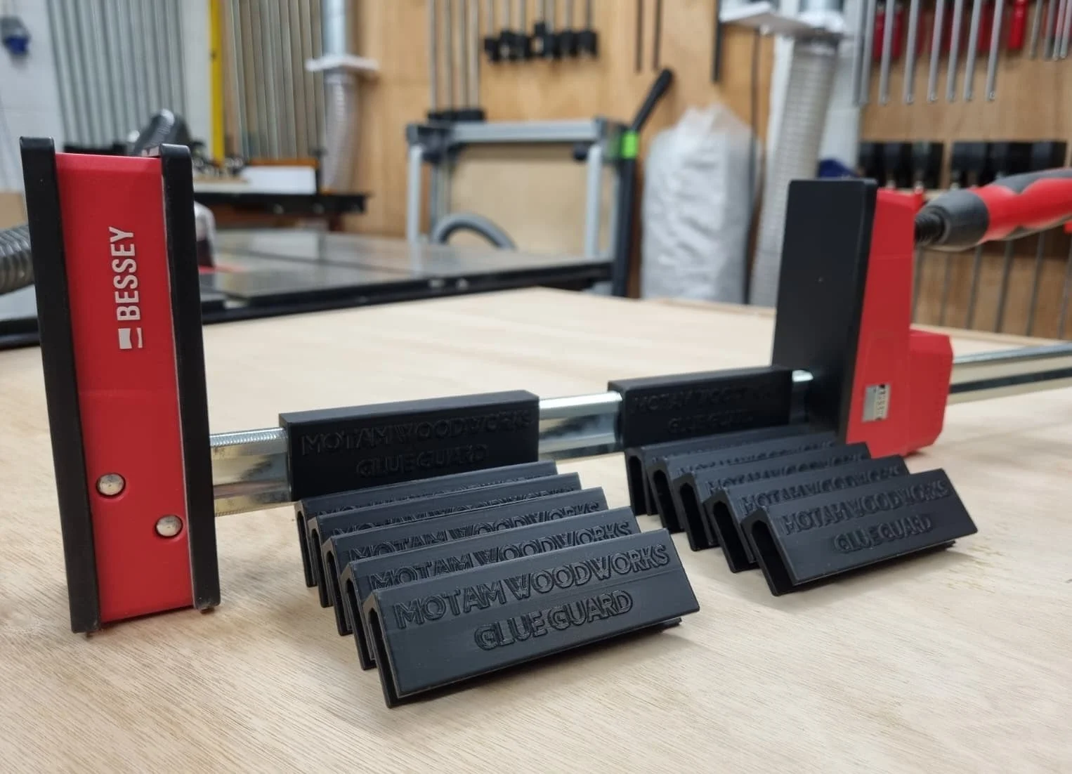 A Bessey K-Body REVO clamp with several Motam Woodworks Glue Guards fitted on the bar, more laid out beside it in a workshop