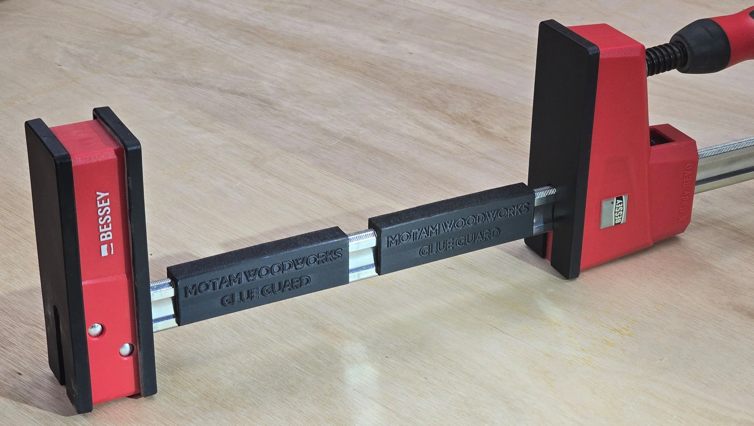 Close-up of a Bessey K-Body REVO clamp bar with two Glue Guard sections snapped in place, embossed "Motam Woodworks Glue Guard"