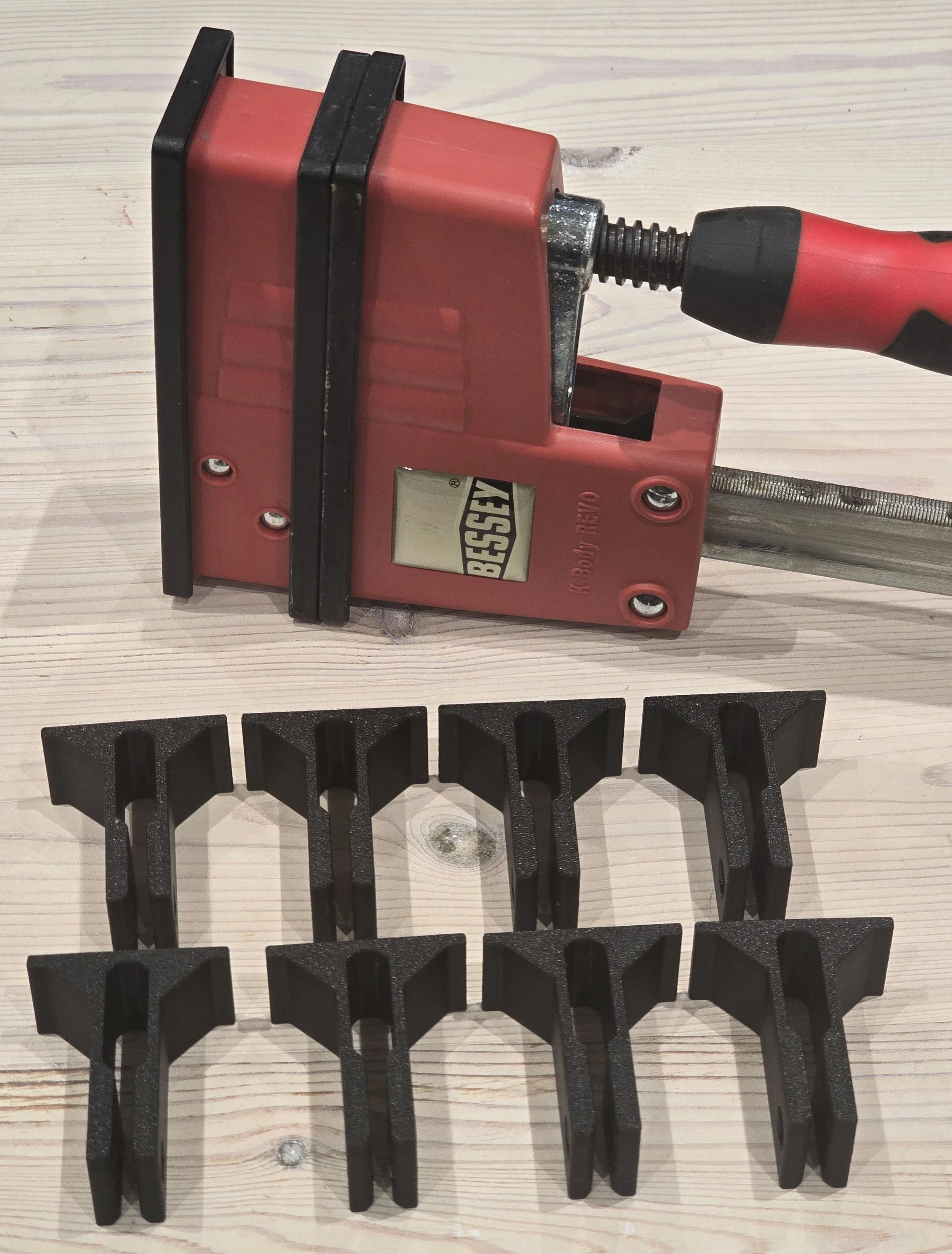 A Bessey K-Body REVO clamp beside eight black bar protection clips laid out on a workbench