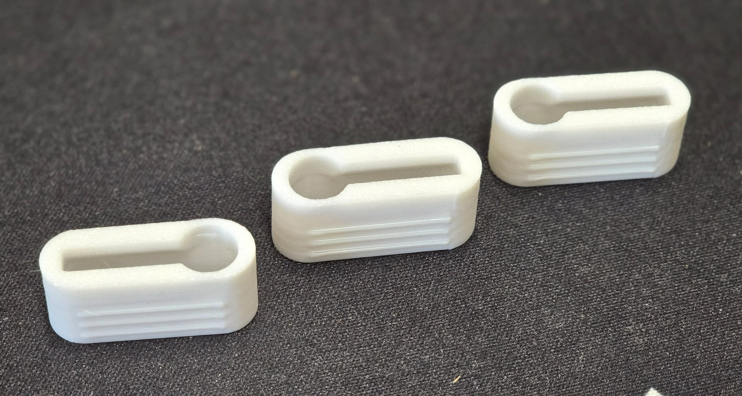 Three white keyhole brackets laid out together on a dark fabric background