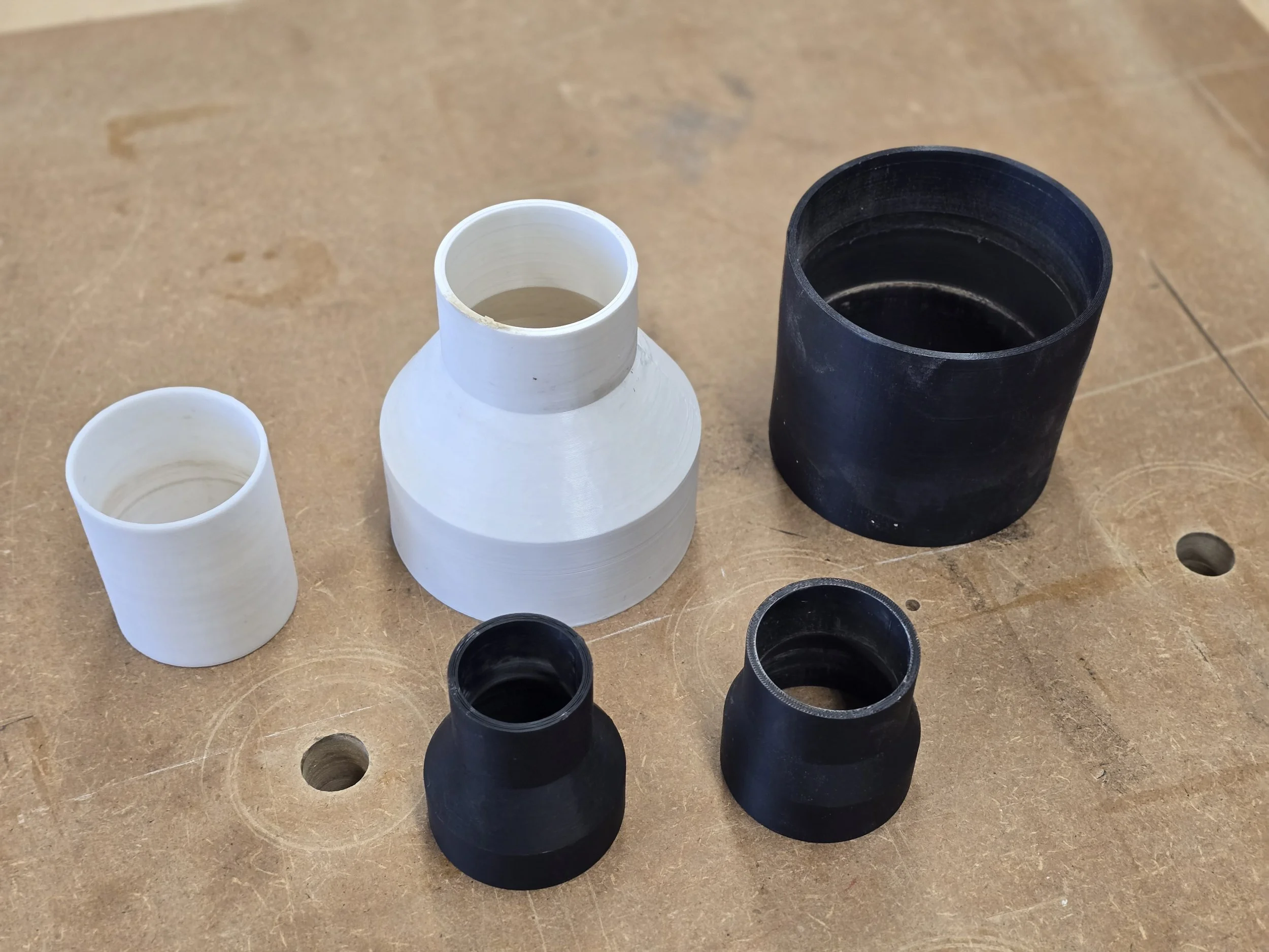 Five sample dust extraction adaptors of different sizes, some straight and some tapered between two diameters, laid out on a workbench