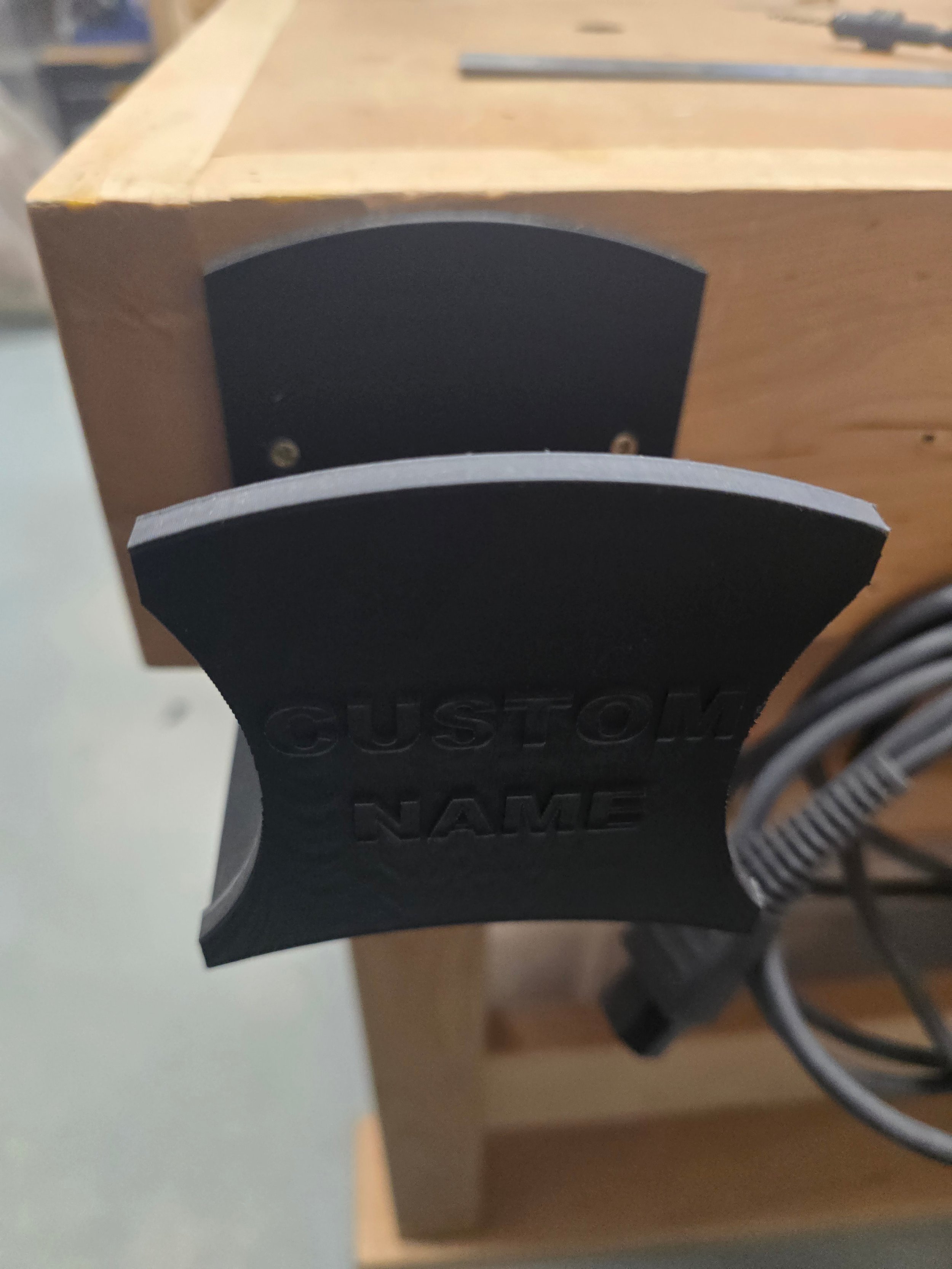 An empty wall mount bracket mounted on a workbench corner, embossed "Custom Name"