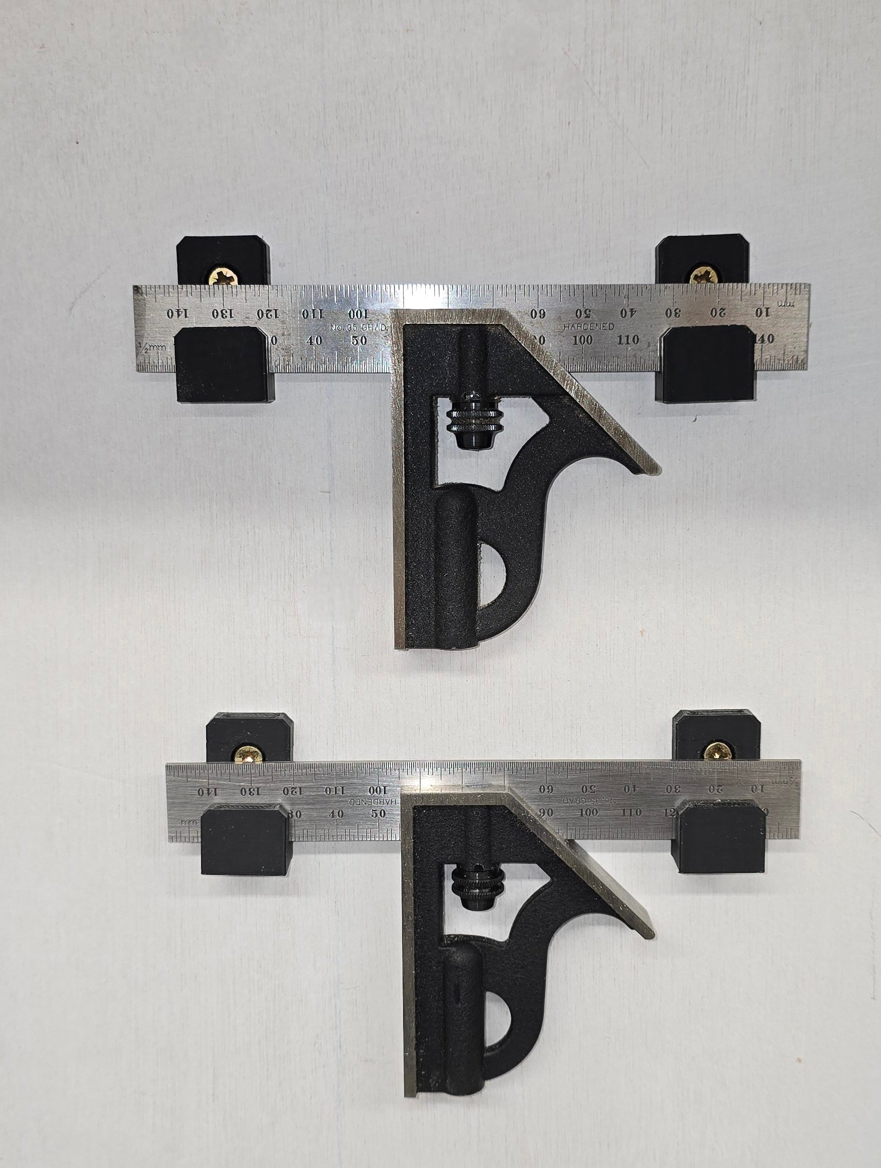 Two combination squares mounted vertically on wall brackets against a plain background