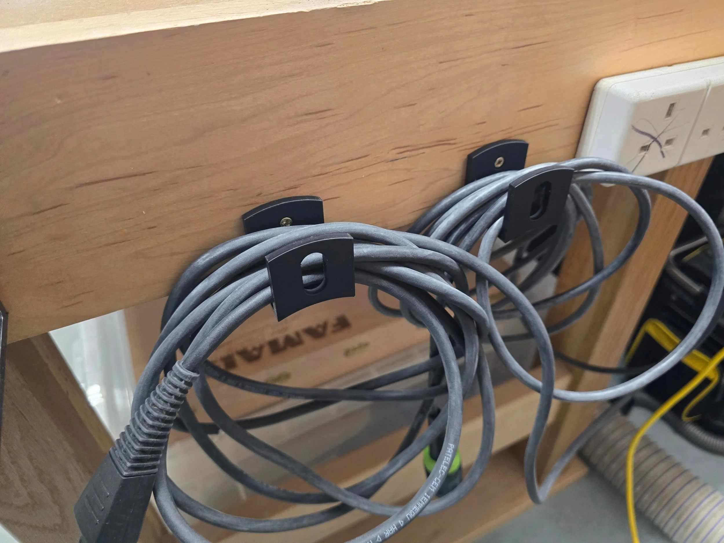Two cable wall hooks screwed to the underside of a workbench, each holding a coiled power cable