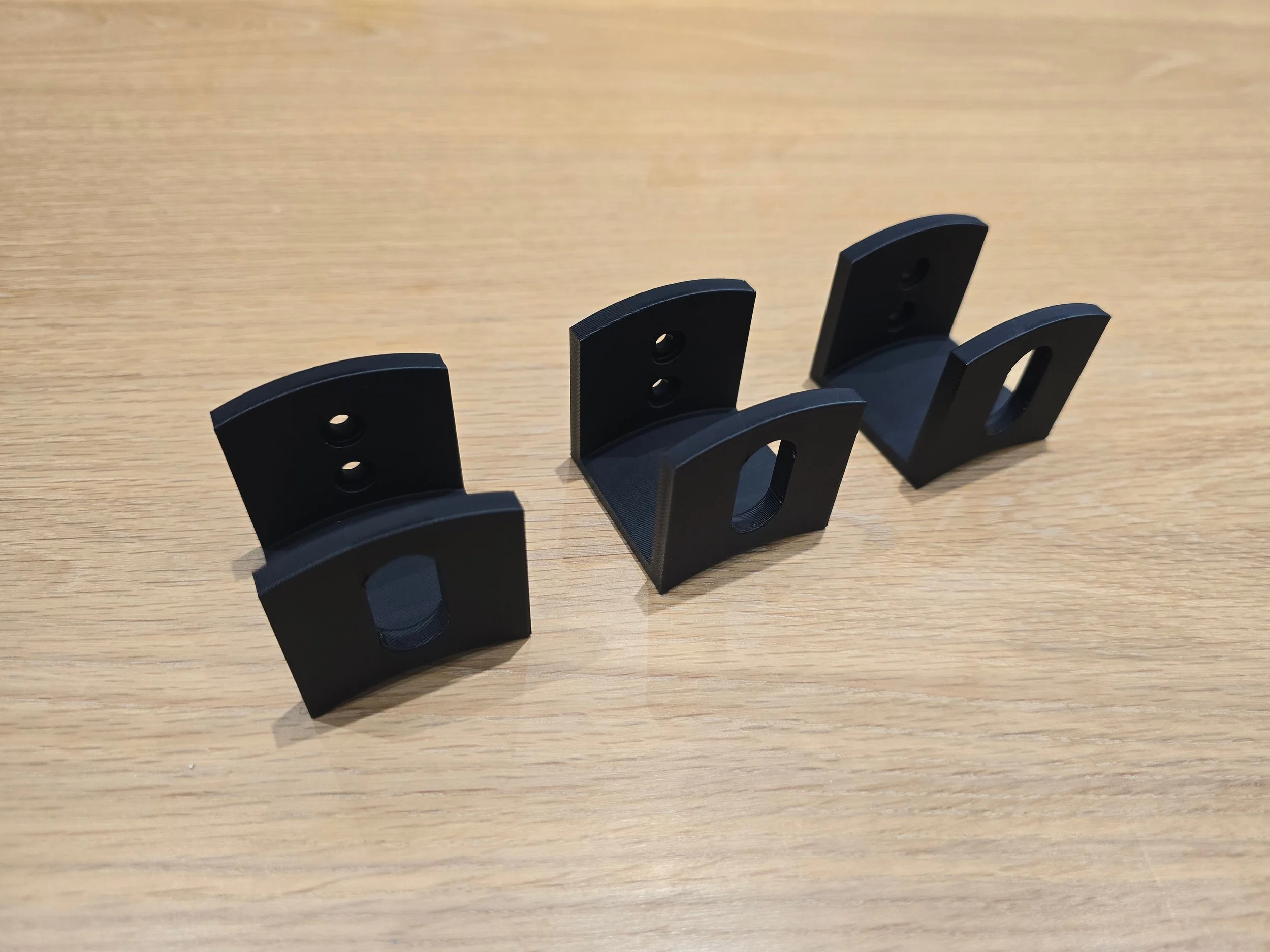 Three unmounted cable wall hooks laid out on a workbench, showing the two mounting holes on each