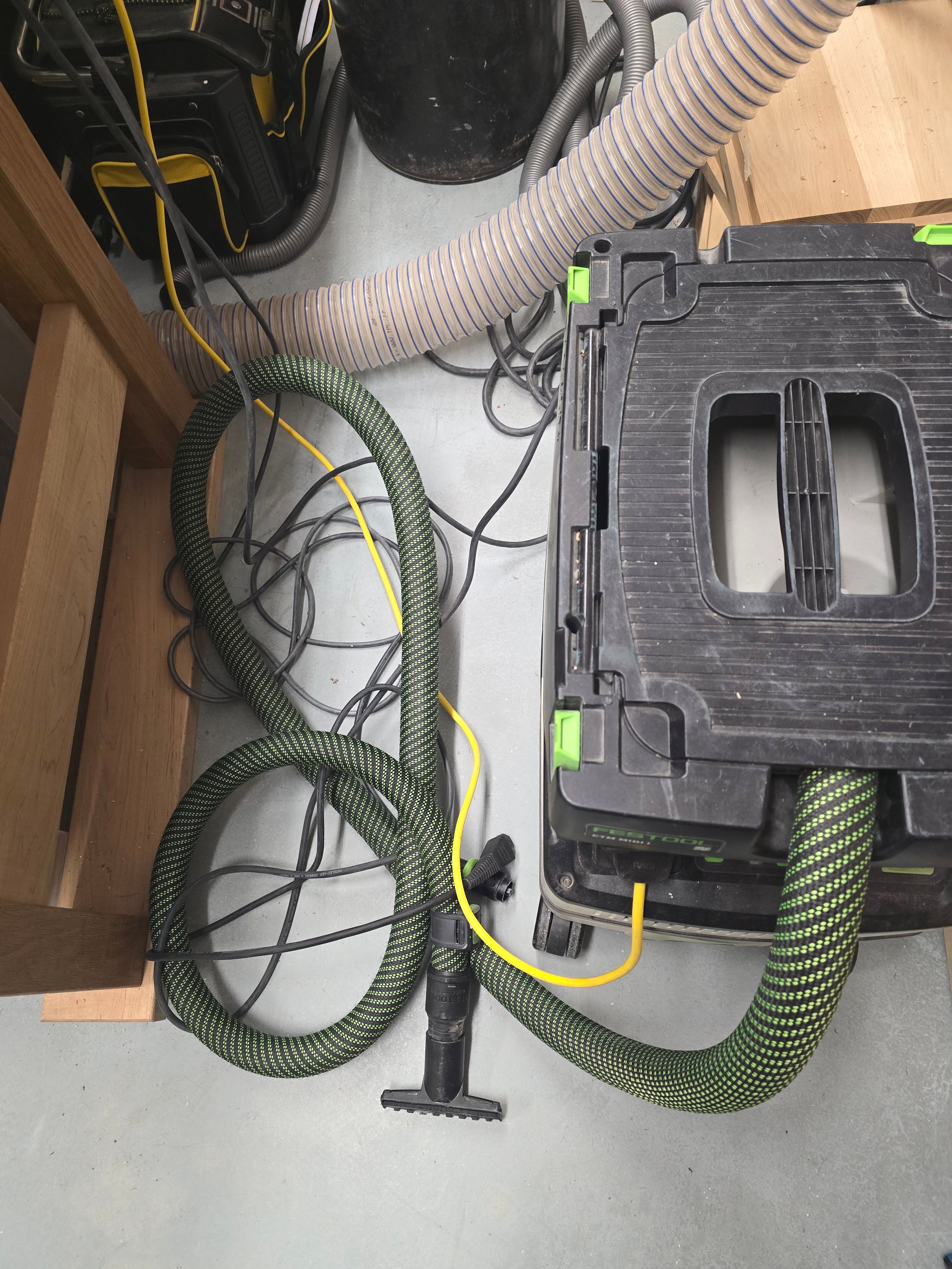 A Festool CTM MIDI dust extractor on the floor with hoses and cables tangled and unmanaged