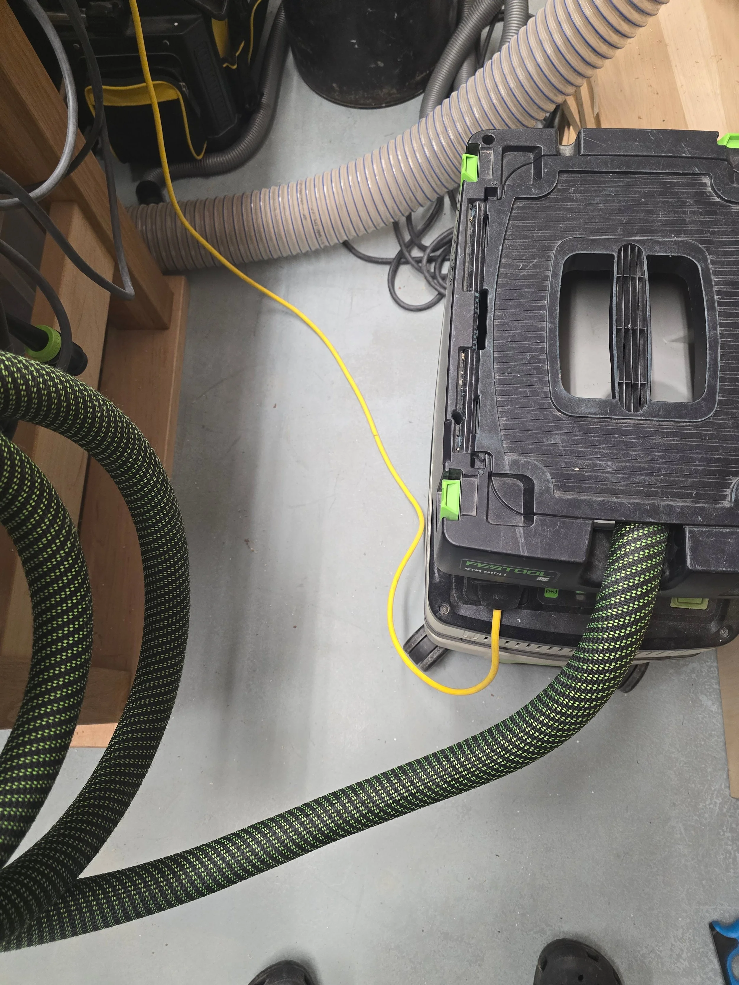 A Festool CTM MIDI dust extractor on the floor with hoses and cables tided up