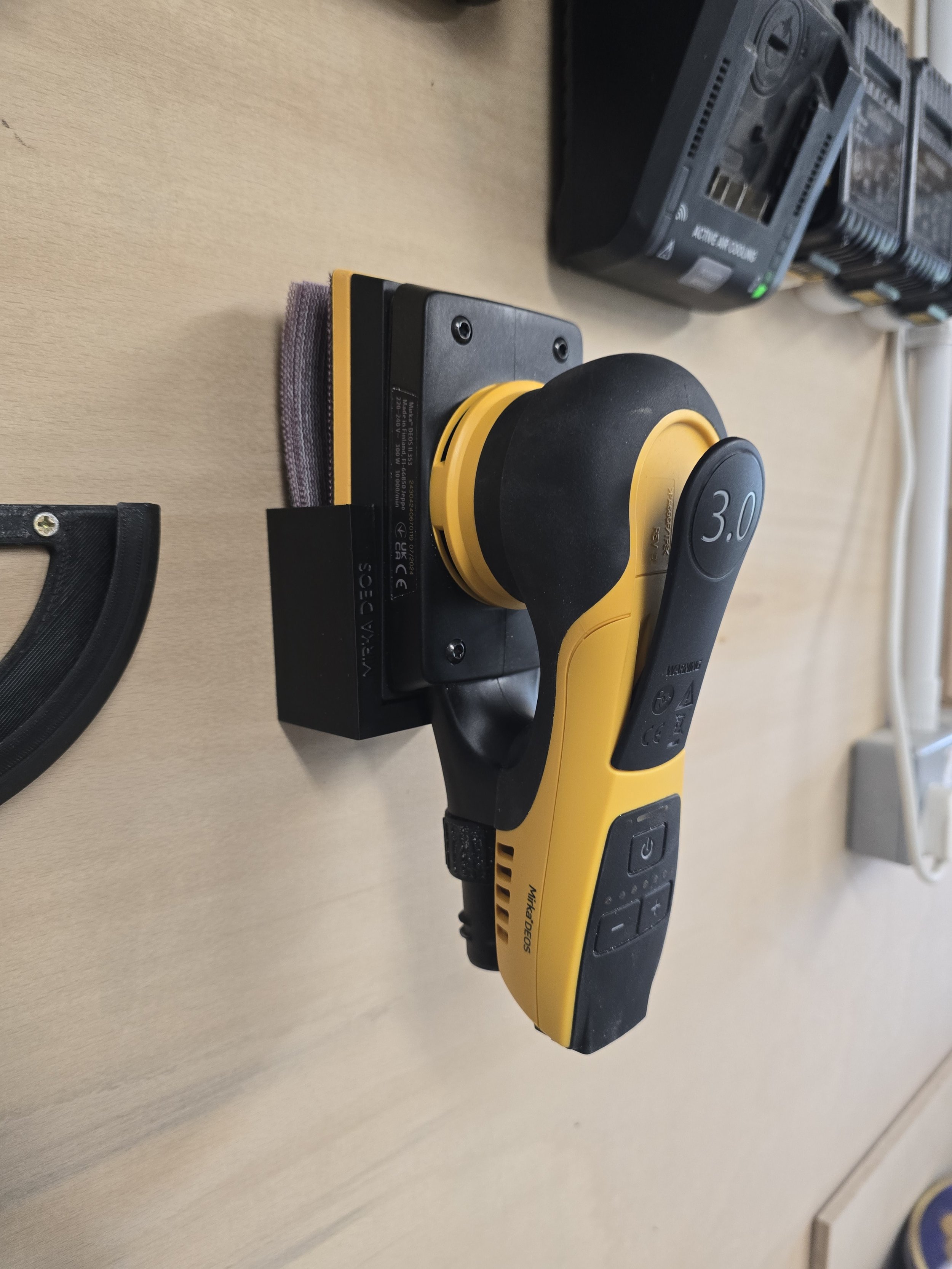 A Mirka DEOS 353 sander held in its wall mount bracket, with a stack of sanding discs alongside