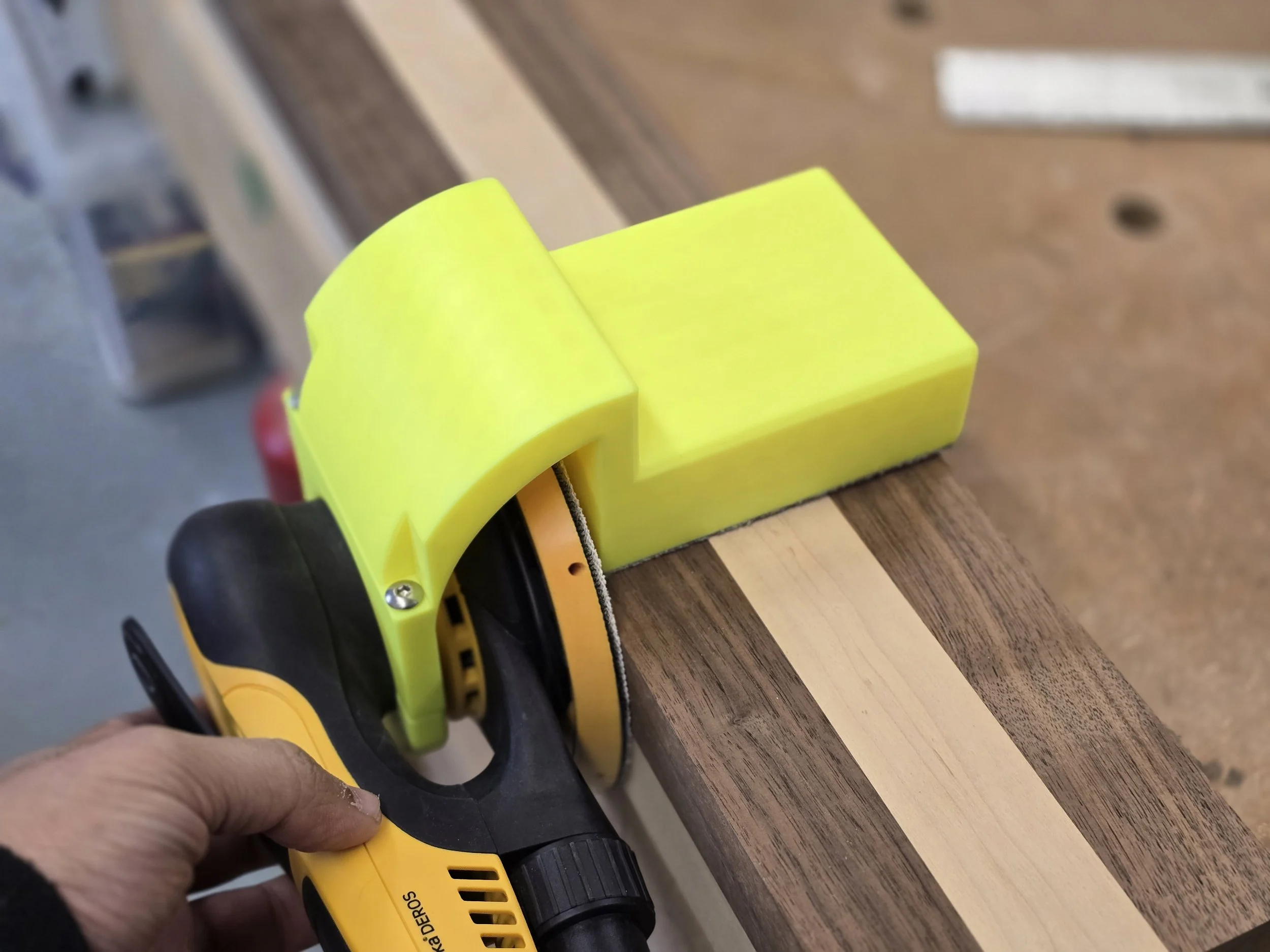 The Motam edge guide fitted to a Mirka DEROS sander, sanding the edge of a striped wooden board
