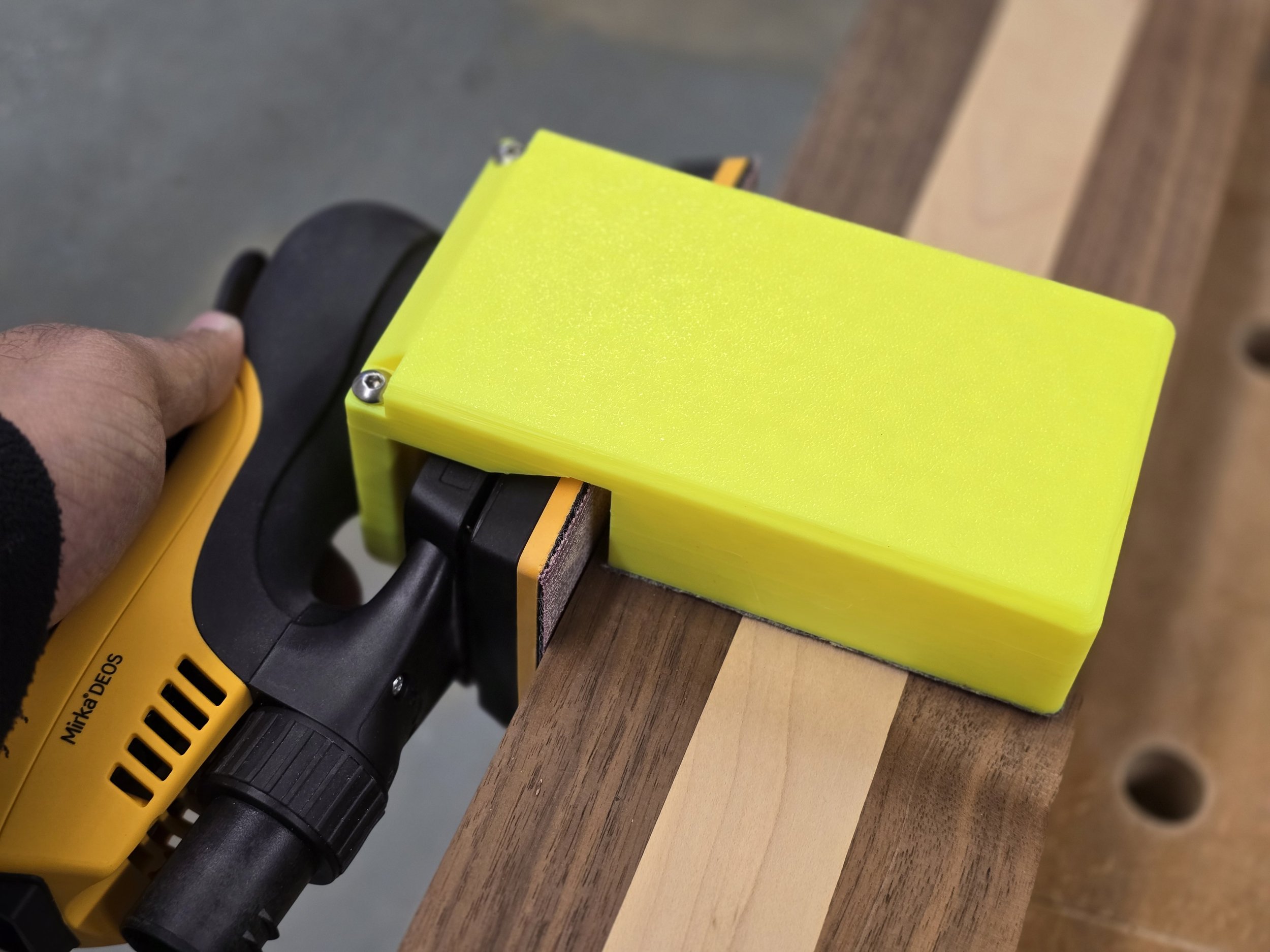 The Motam edge guide fitted to a Mirka DEOS sander, sanding the edge of a striped wooden board