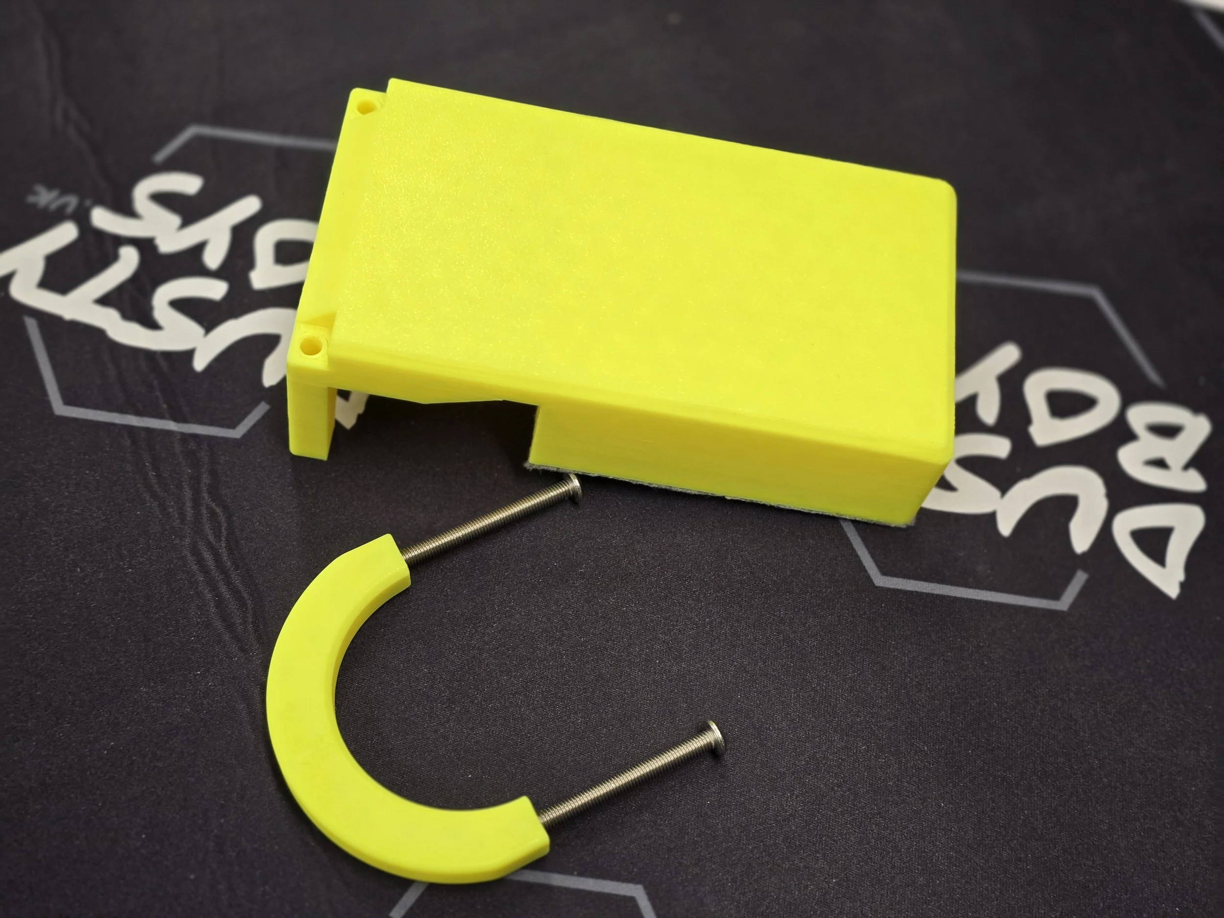 The Deos-variant edge guide disassembled, showing the rectangular felt-padded body, curved bracket, and two screws