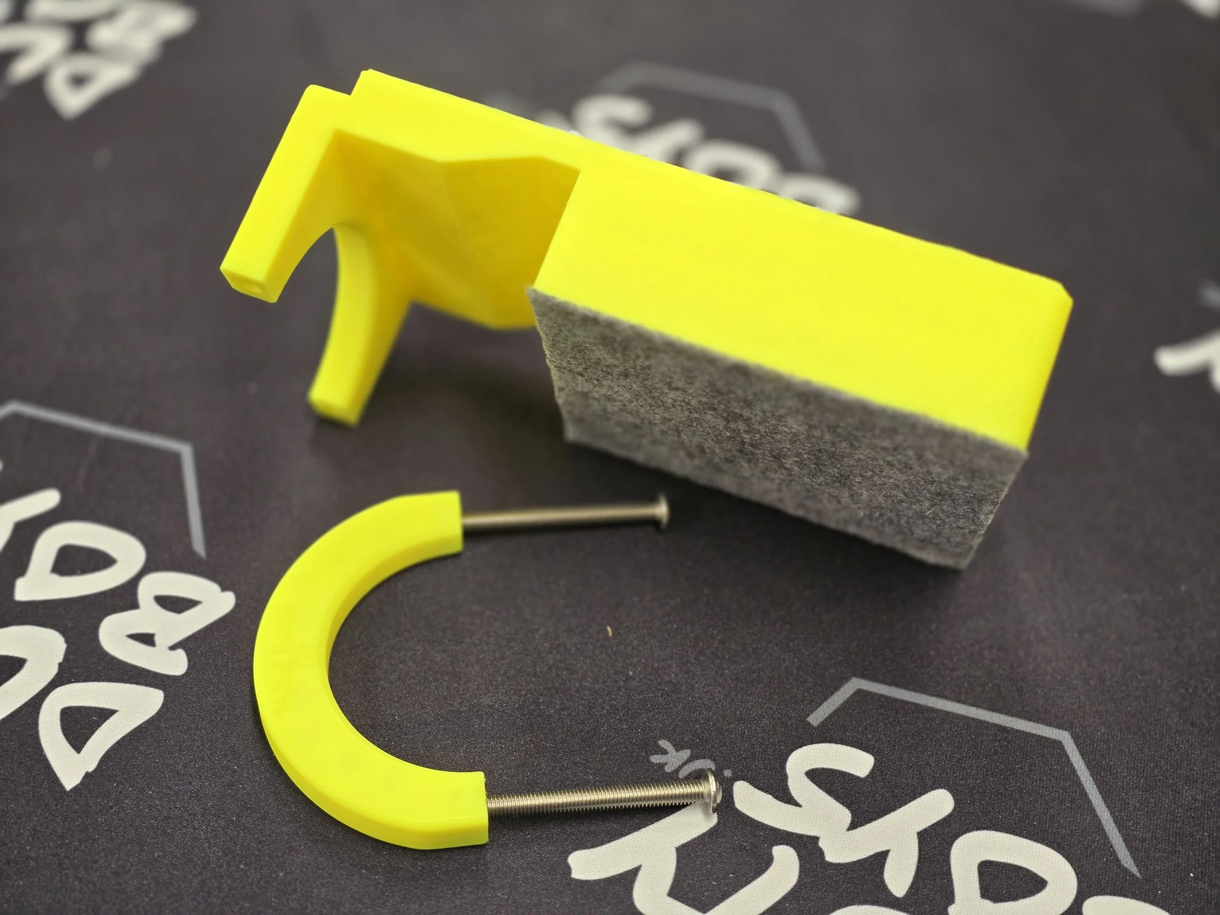 The edge guide disassembled, showing the felt-padded body, curved mounting bracket, and two screws
