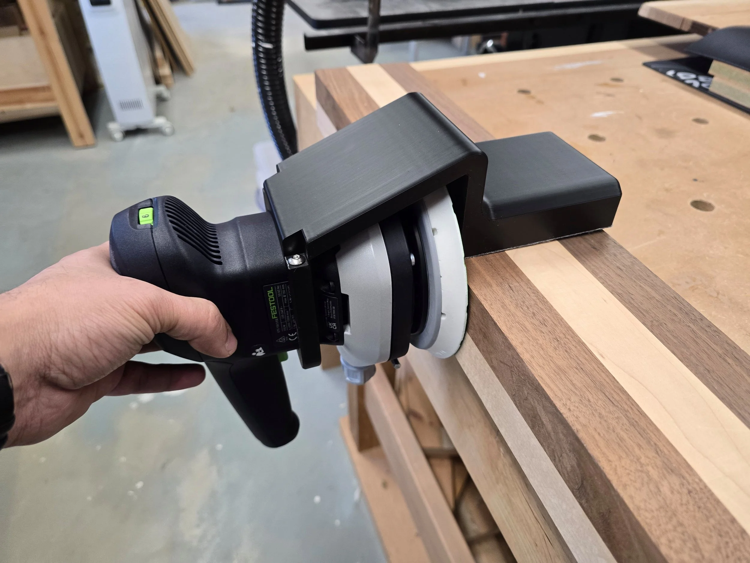 The Motam edge guide fitted to a Festool ETS sander, sanding the edge of a striped wooden board