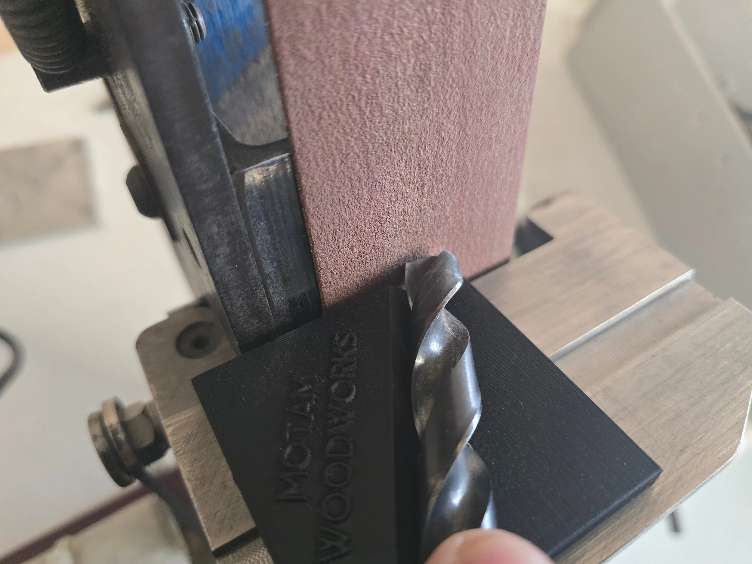 A drill bit held against the sanding belt on the Robert Sorby ProEdge system, guided by the 3d printed Motam woodworks drill bit jig