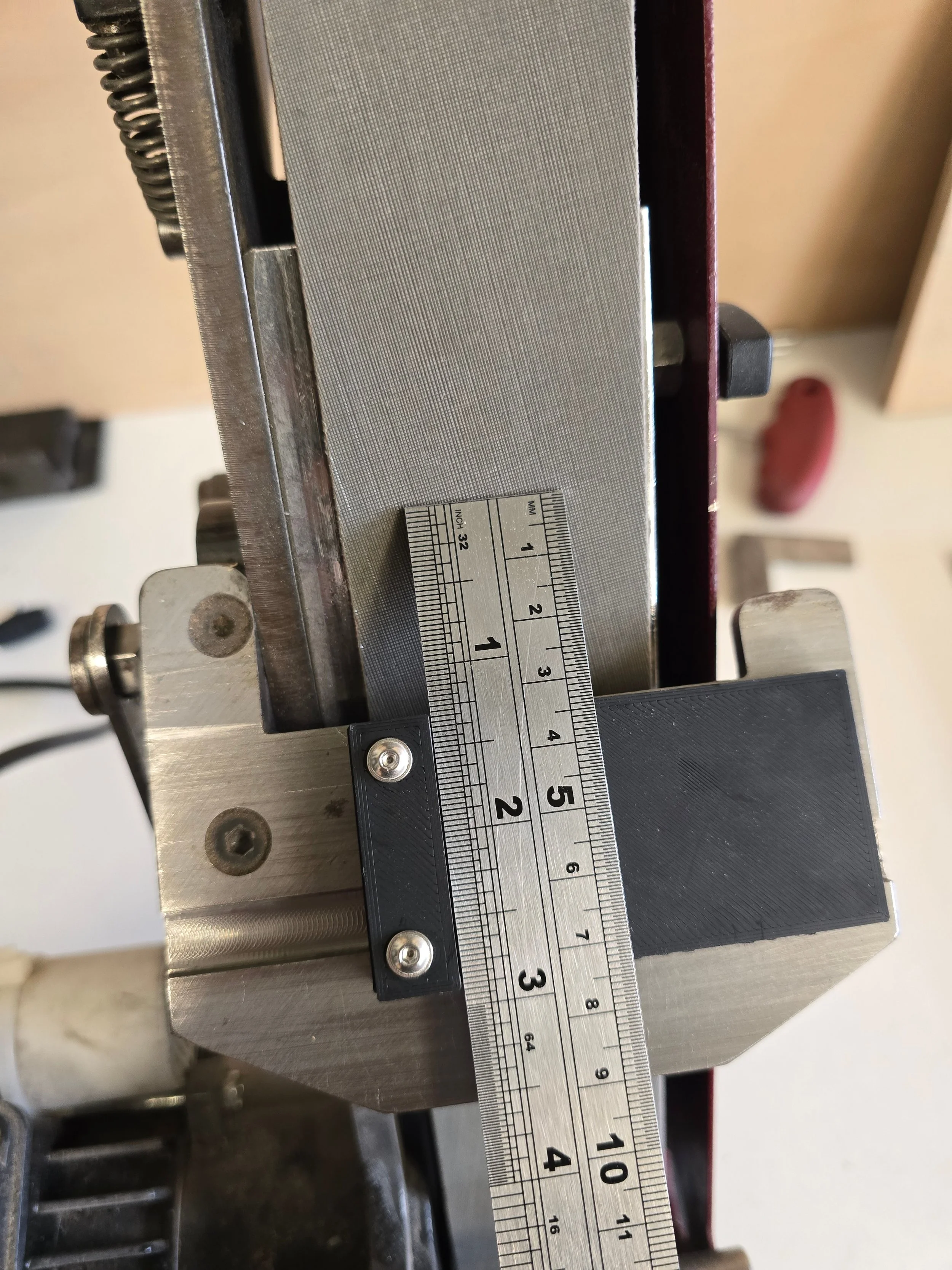 steel ruler held against the jig showing roughly 1 inch (25mm), demonstrating how much closer to the belt it reaches compared to the standard PESQW model
