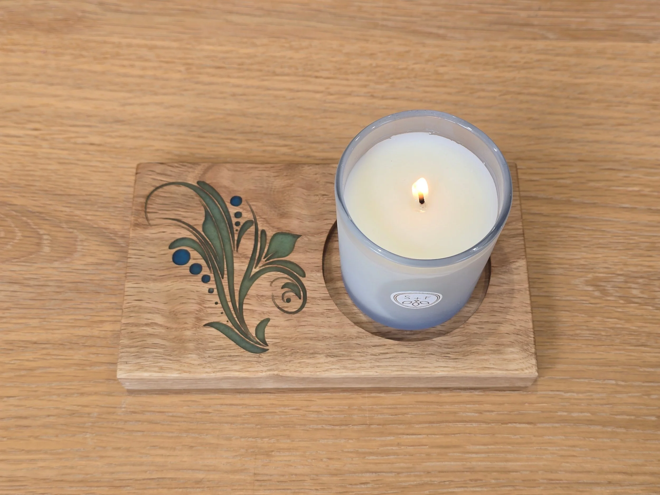 Close-up overhead view of the oak candle holder's floral resin inlay with a lit candle in place