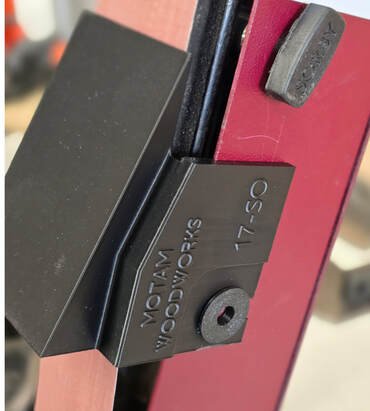 Close-up of a woodworking clamp securing a wooden piece to a table.