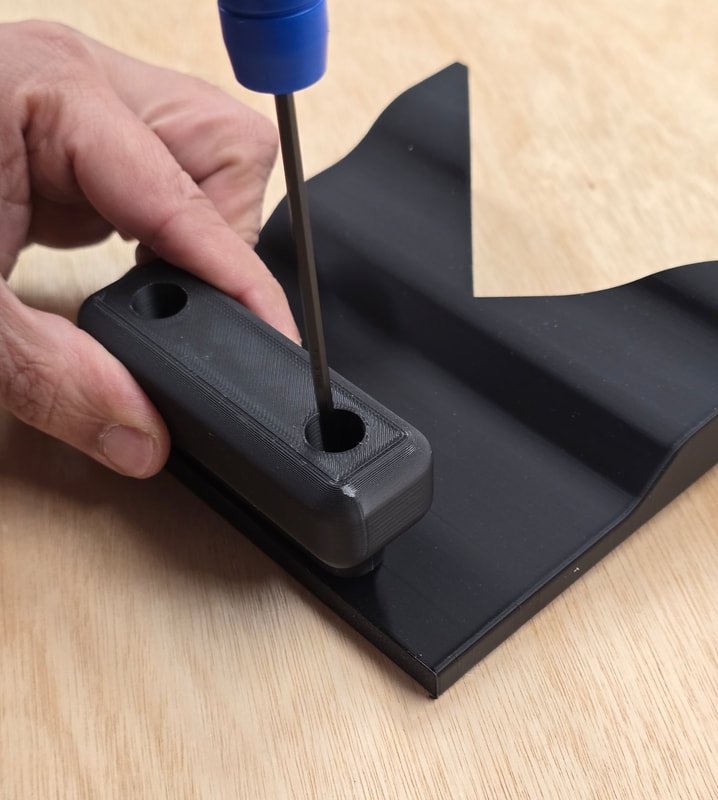 A person using a Phillips-head screwdriver to insert a screw into a black plastic device resting on a black tray.