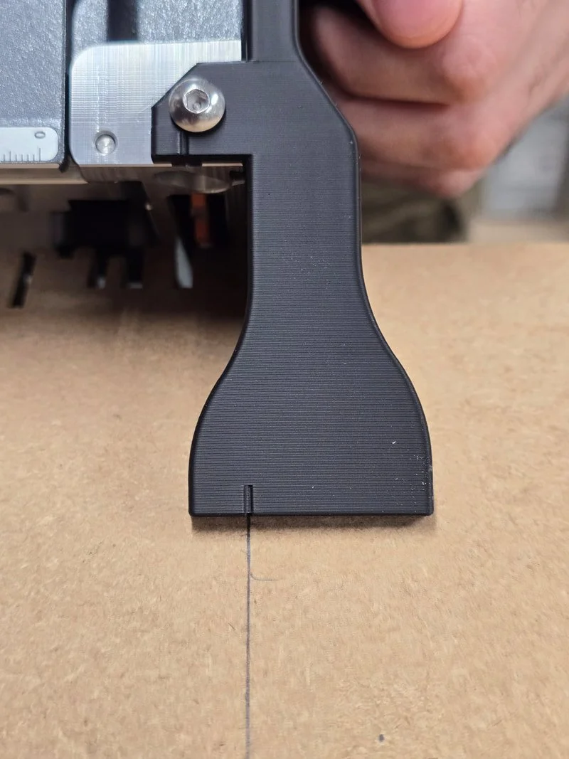 Close-up of a black measuring tool or gauge placed on a piece of wood, with a person's hand holding part of the device visible in the background.