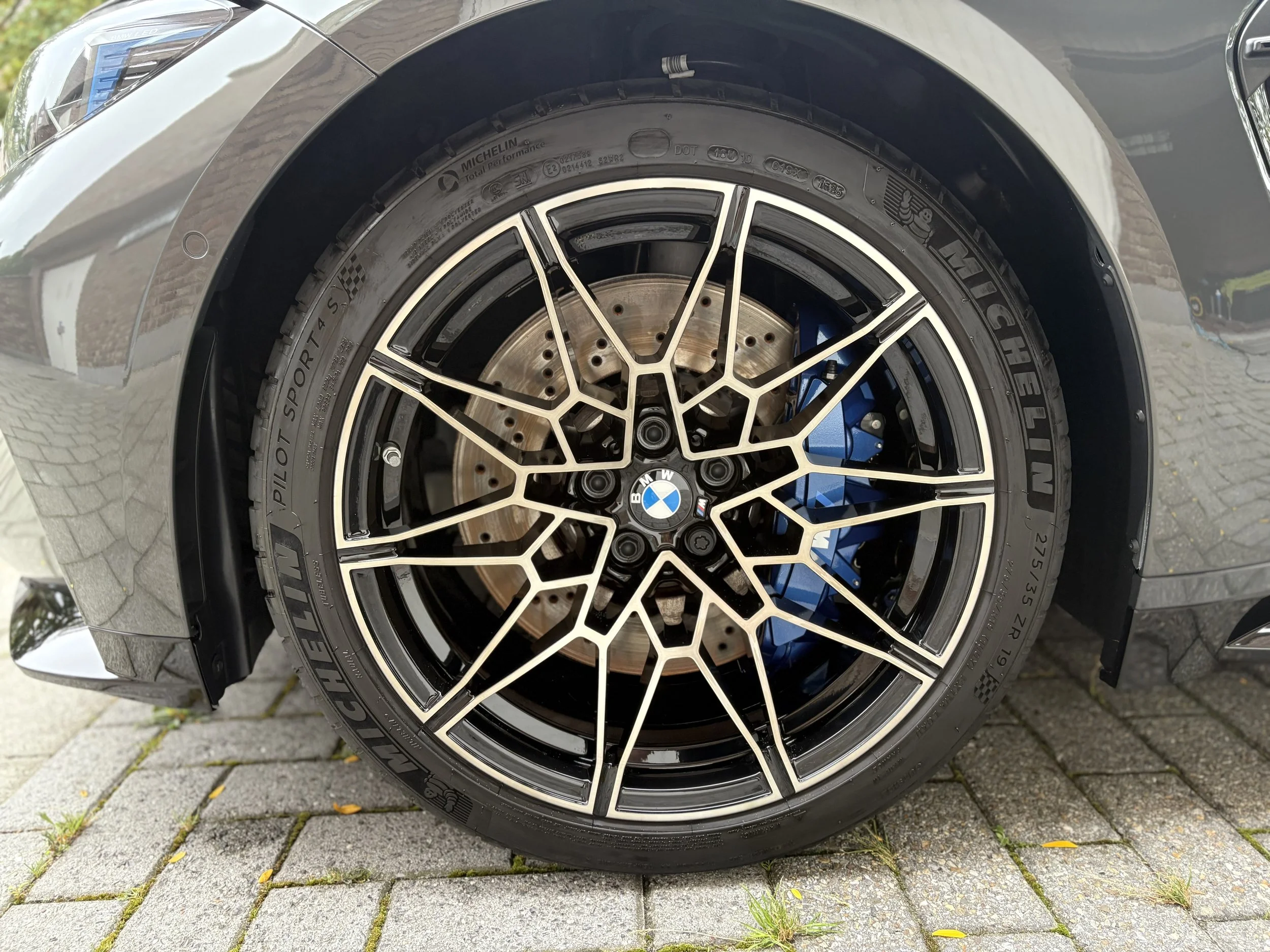 Close-up van een autoband met een geavanceerd Dunlop Wheel Tire en een BMW-model logo, gemonteerd op een velg met een ingewikkeld design, bevestigd aan een BMW auto, geparkeerd op een stenen oprit.