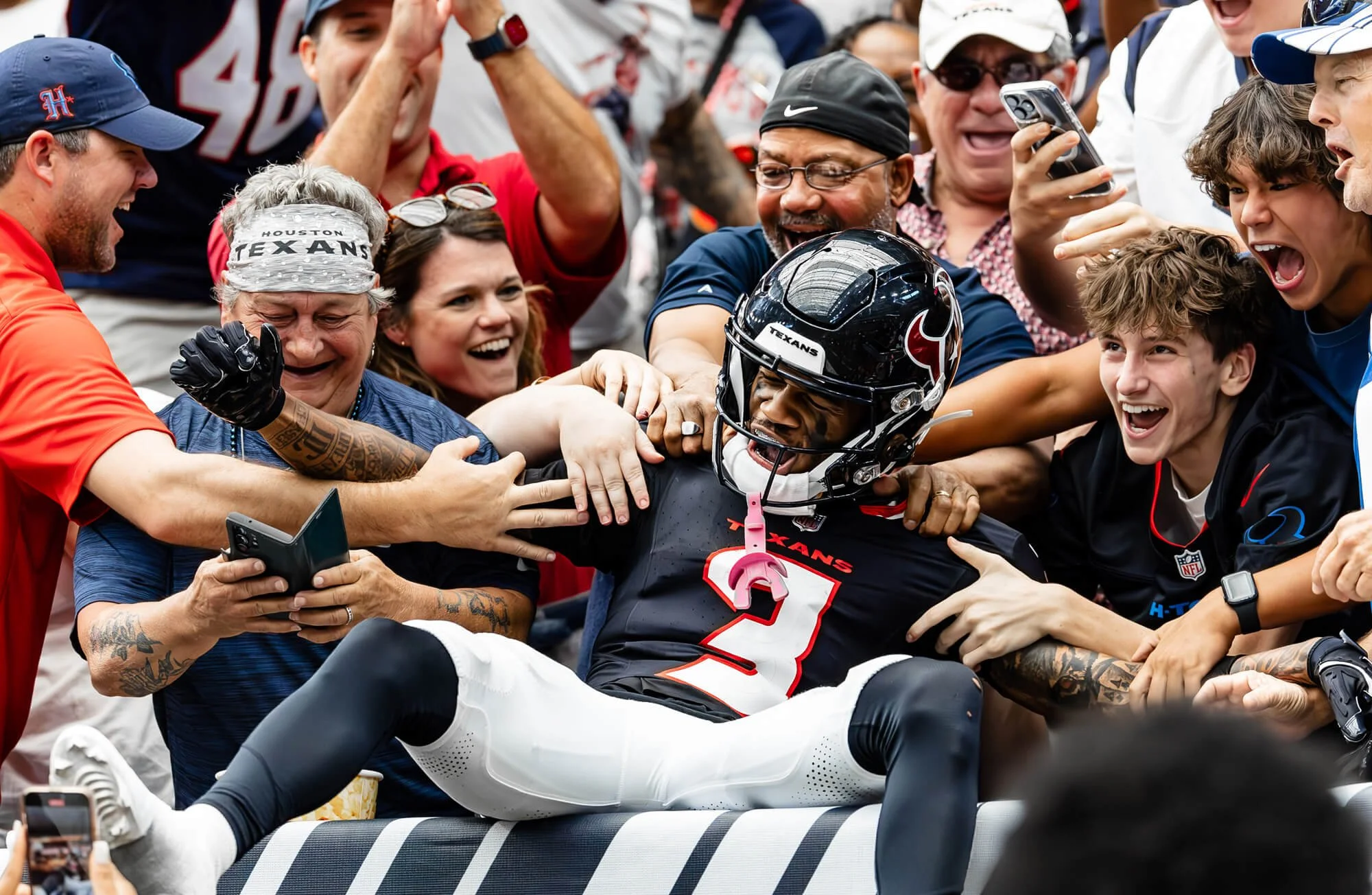 Football player in uniform sitting on the ground surrounded by happy fans and teammates, celebrating.