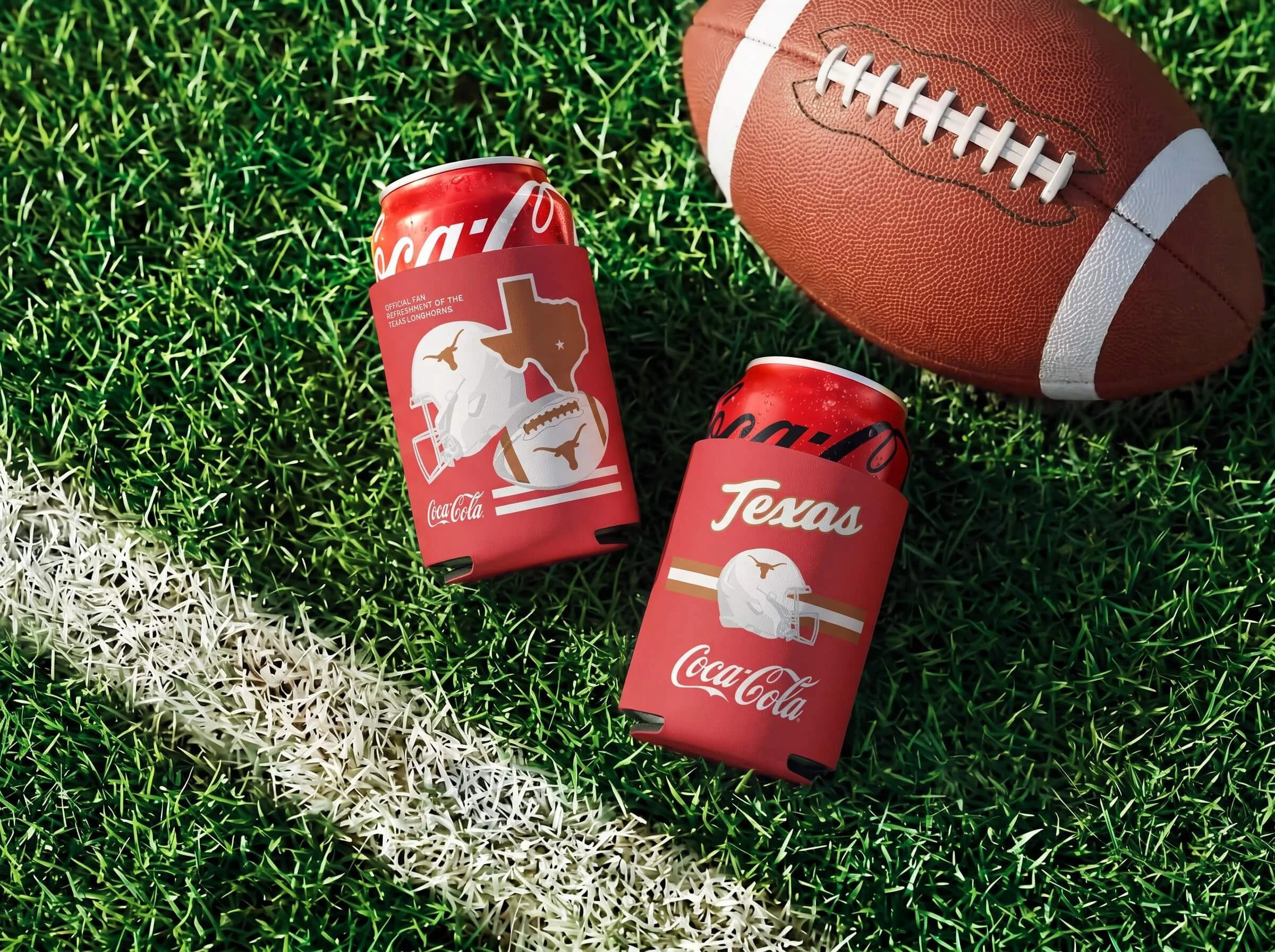 An American football lying on a green field next to red Coca-Cola cans with Texas Longhorns logos and a Texas state outline design on the cans.