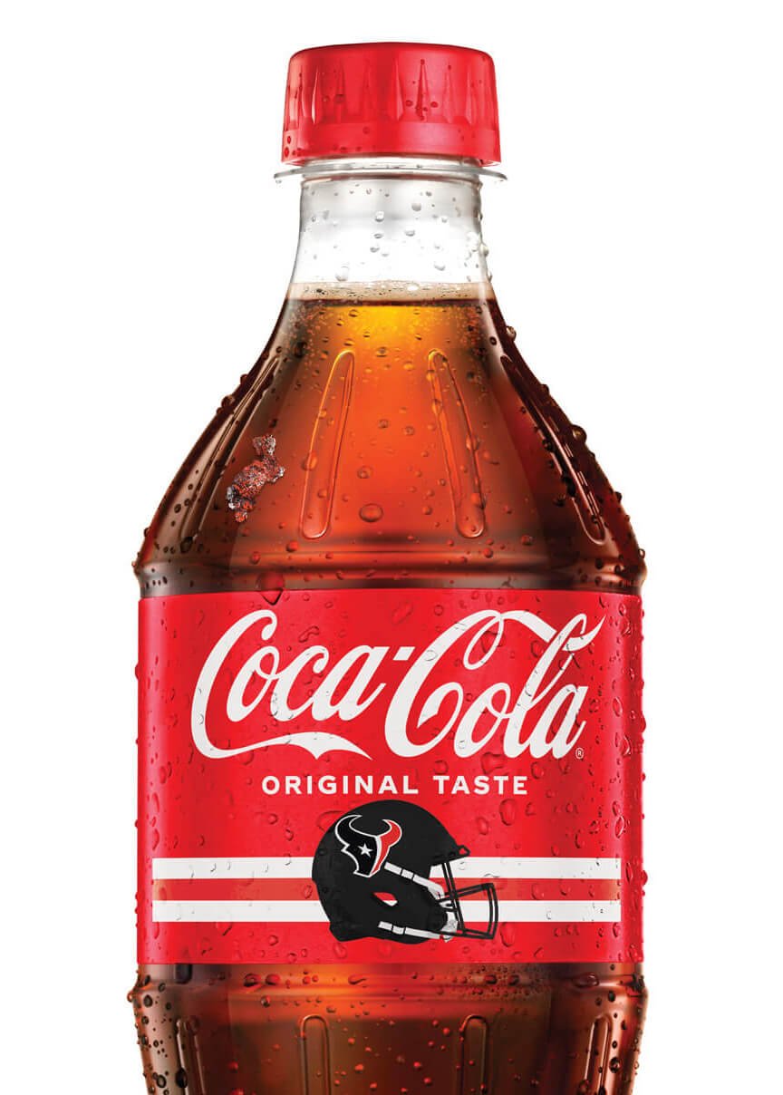 A bottle of Coca-Cola with a red label, featuring the Coca-Cola logo, the words "Original Taste," and the Houston Texans football team logo, with droplets of condensation on the bottle.