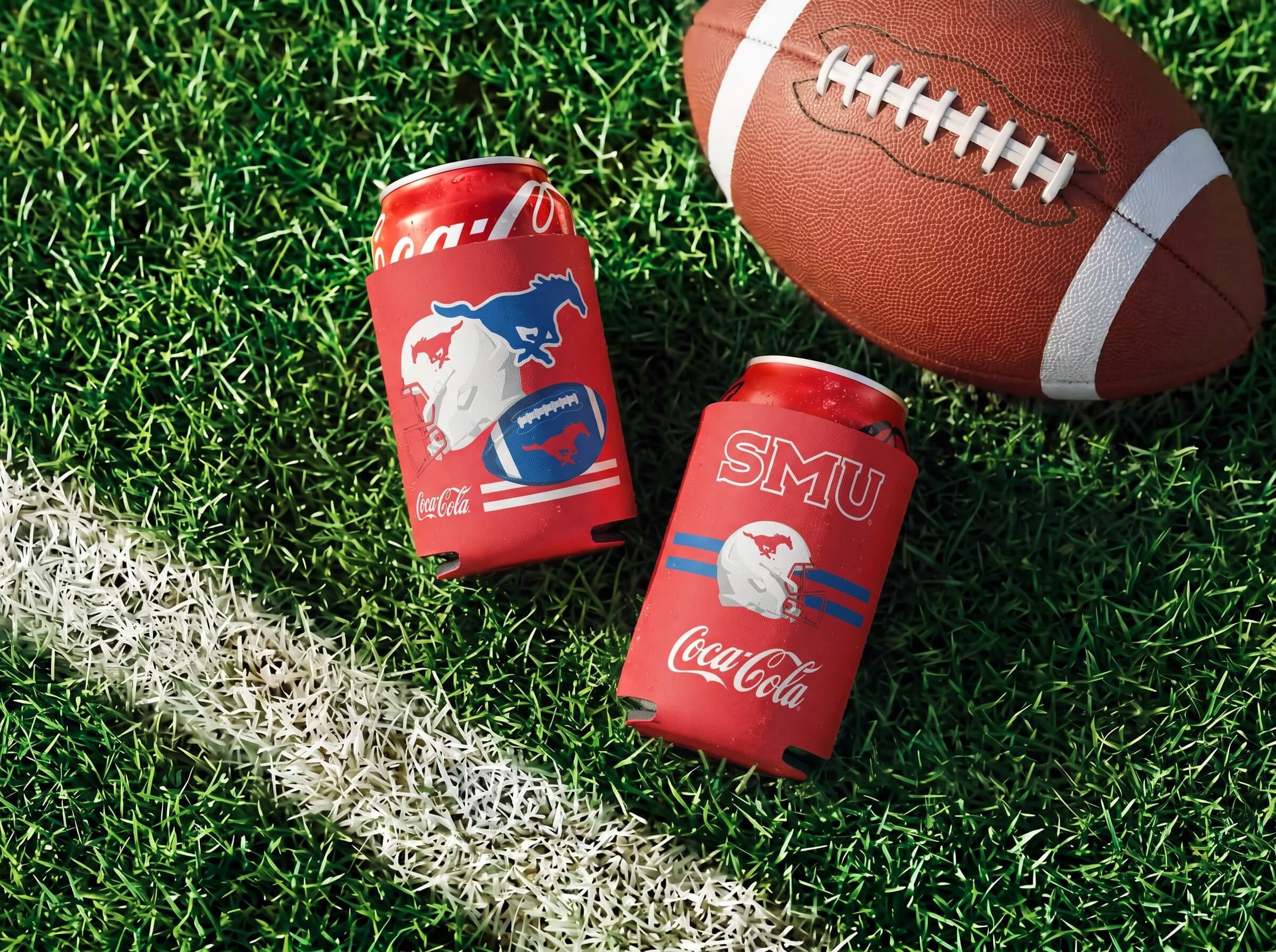 A football lying on a grass field with white and green lines, and a can of Coca-Cola with a red blanket or cozy around it with