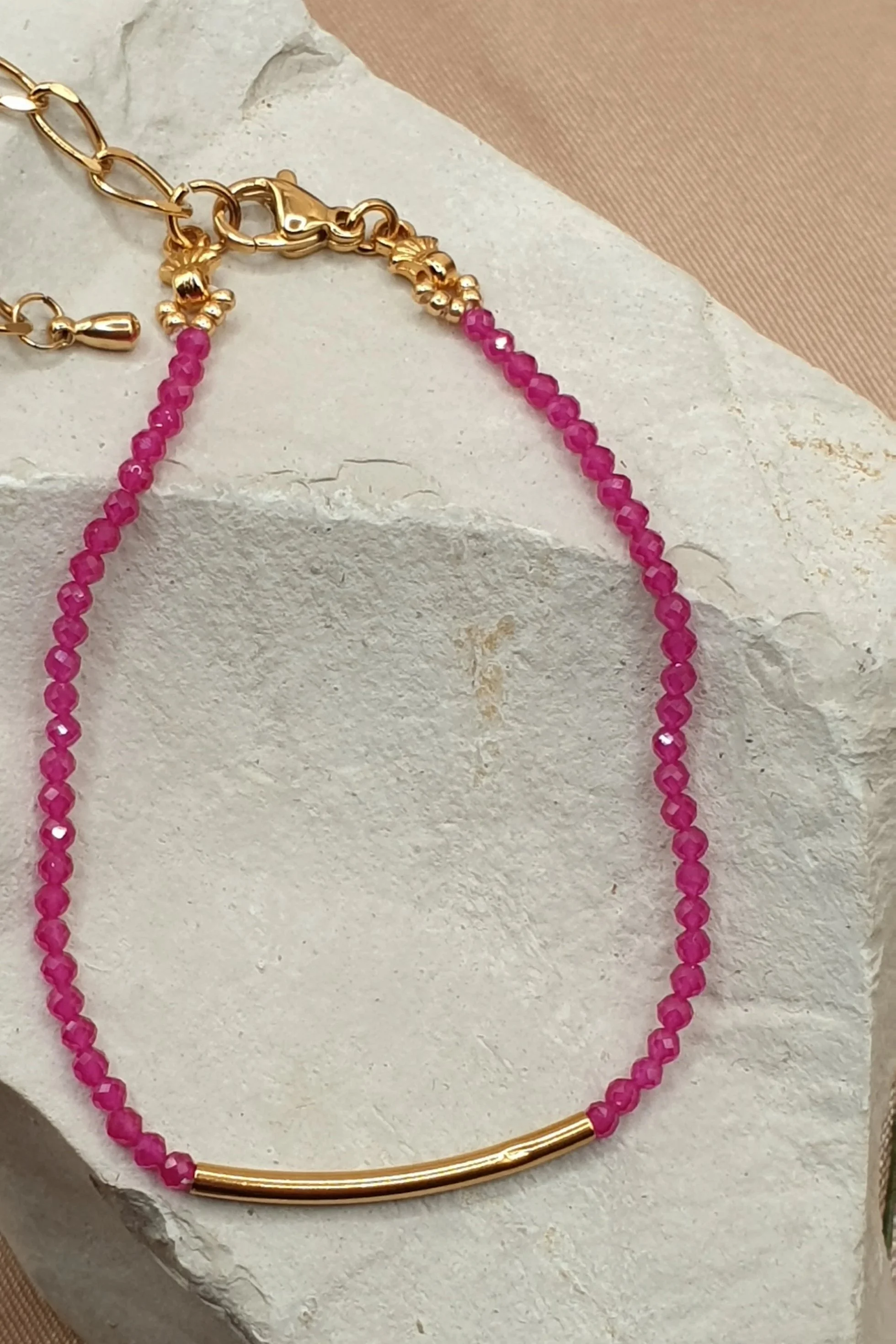 Bracelet Fil de Rubis en pierres roses facettées avec tube central doré, posé sur une pierre claire