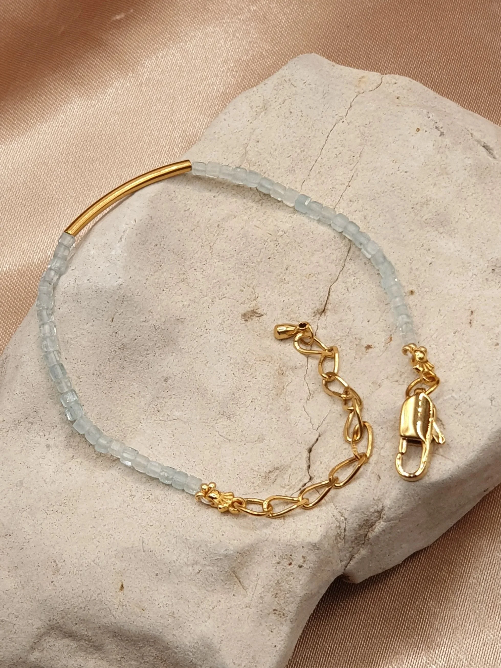 Bracelet Souffle des Lagons posé à plat sur une pierre claire, avec sa chaînette et son fermoir dorés