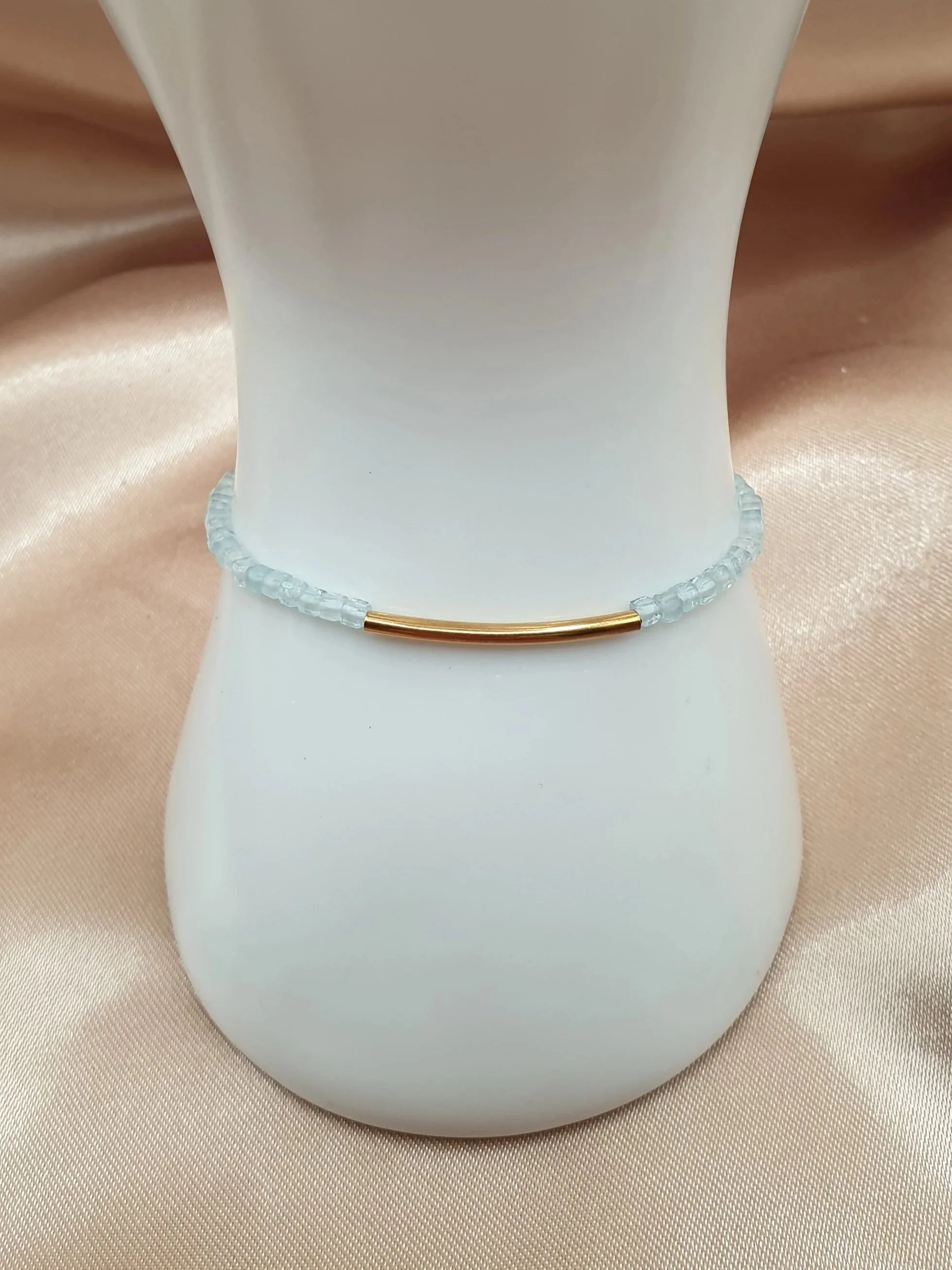 Bracelet Souffle des Lagons en aigue-marine bleu clair avec élément central doré sur un présentoir blanc