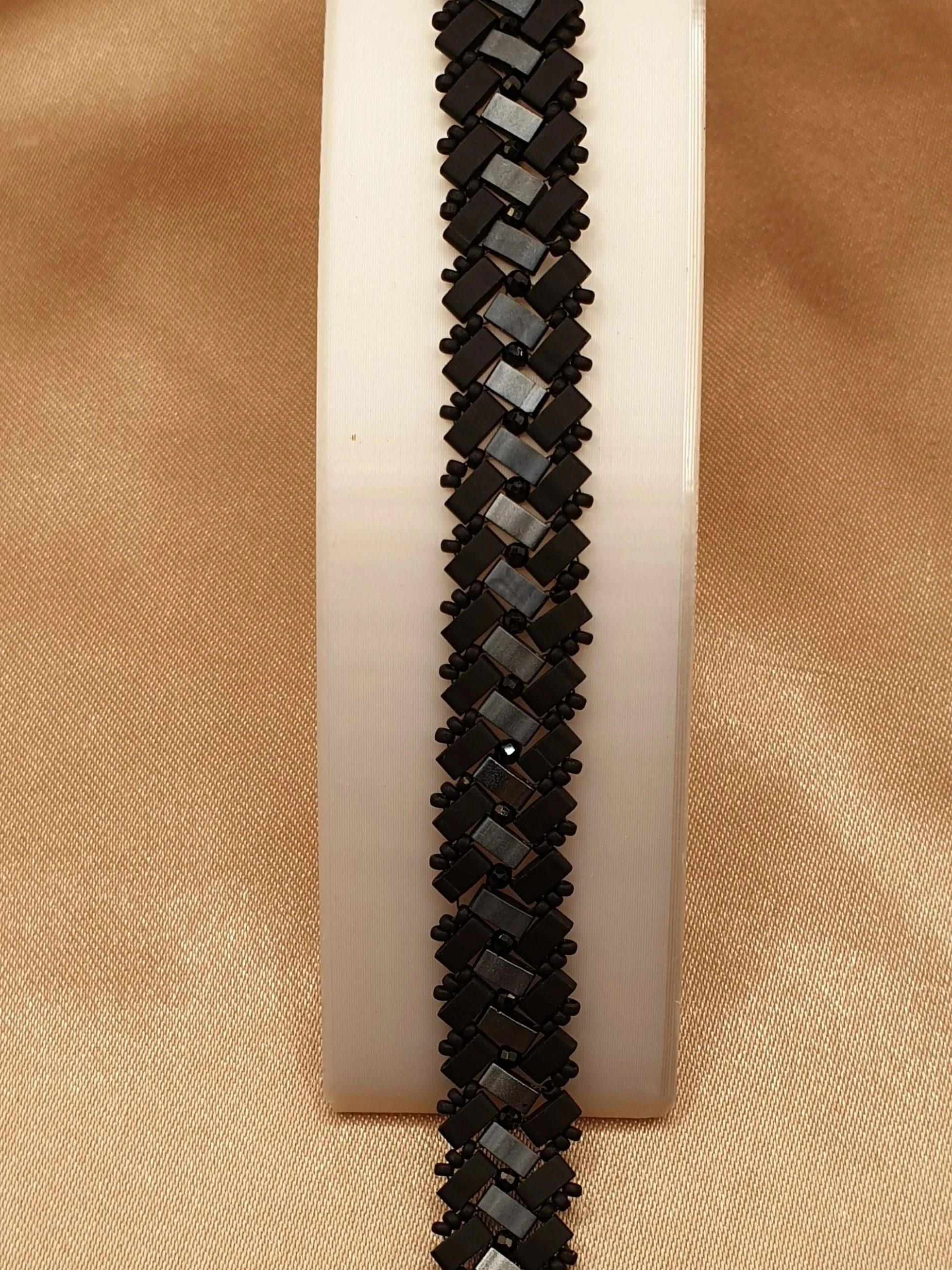 Bracelet Éclipse d’Onyx vu à plat sur un fond beige, motif géométrique noir et gris