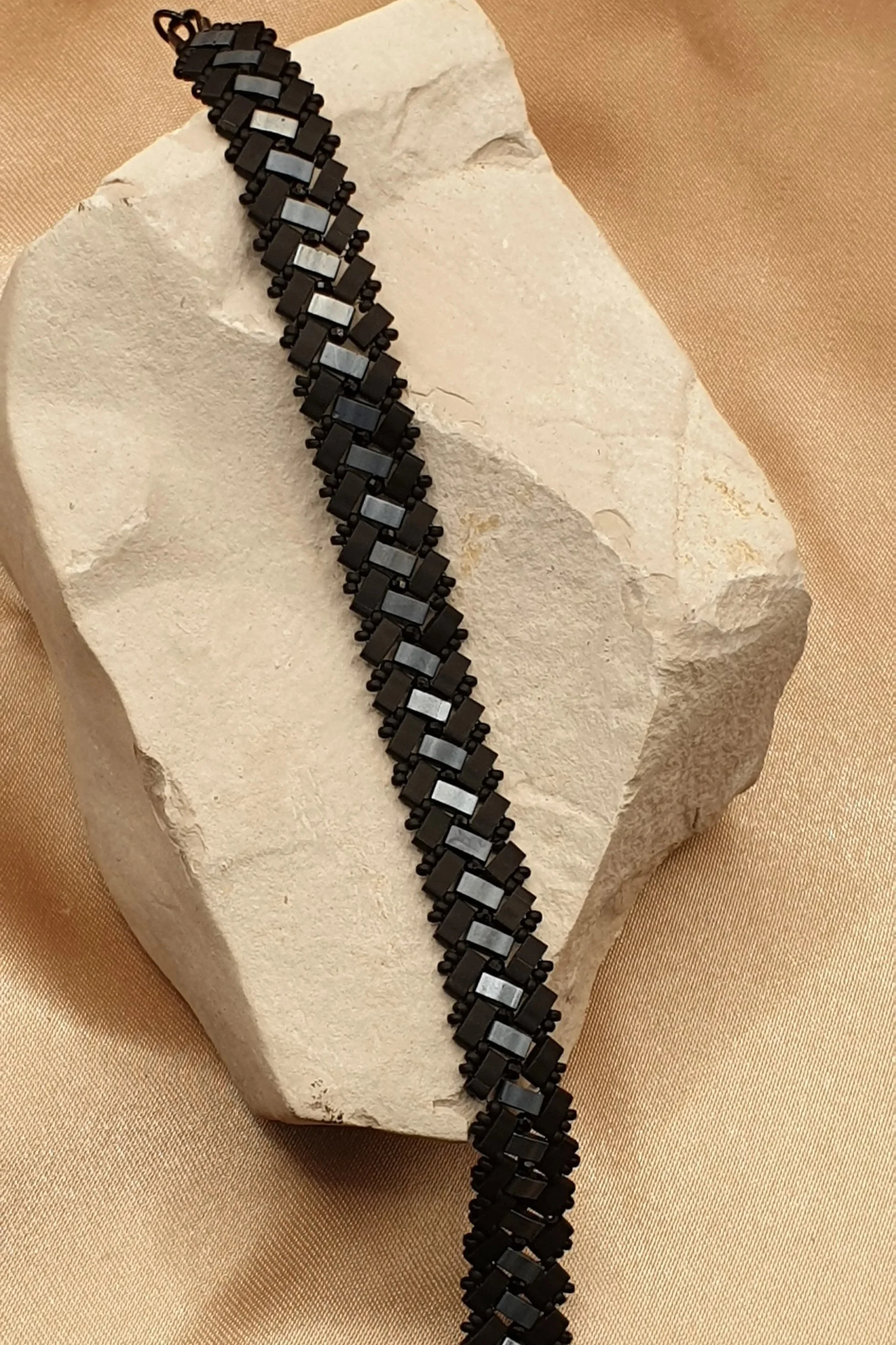 Bracelet Éclipse d’Onyx tissé en perles noires mates et grises métallisées, posé sur une pierre claire