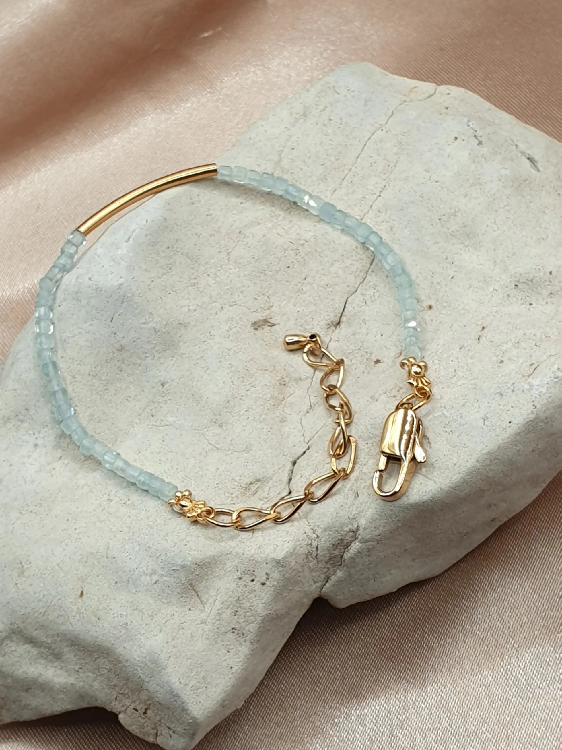 Bracelet Souffle des Lagons en aigue-marine bleu clair avec tube central doré, posé sur une pierre