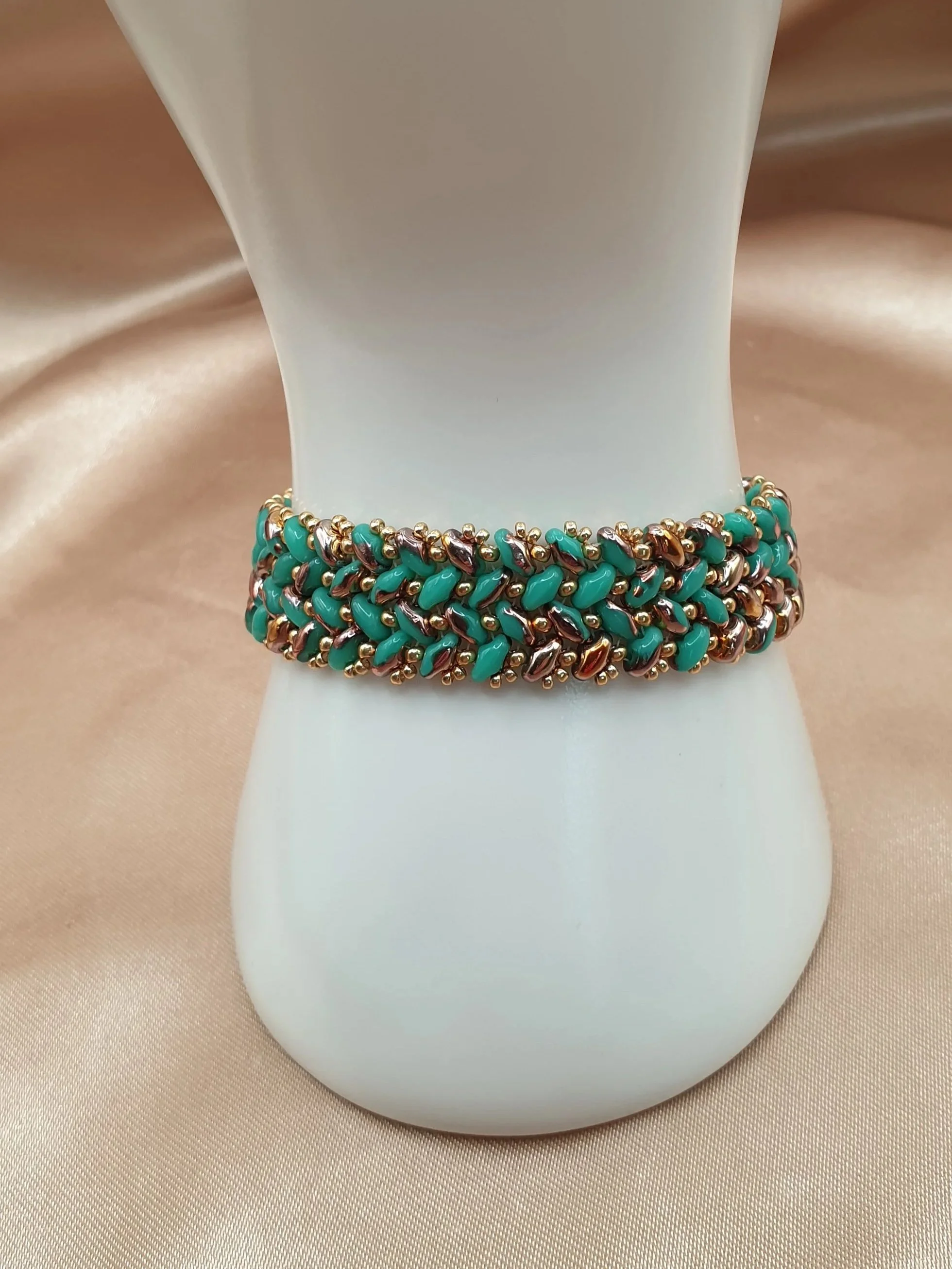 Bracelet Oasis d’Or en perles vert turquoise et dorées autour d’un présentoir blanc