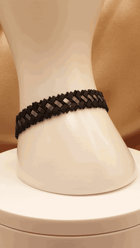 Bracelet Éclipse d’Onyx autour d’un présentoir blanc, vue de profil du tissage noir et gris