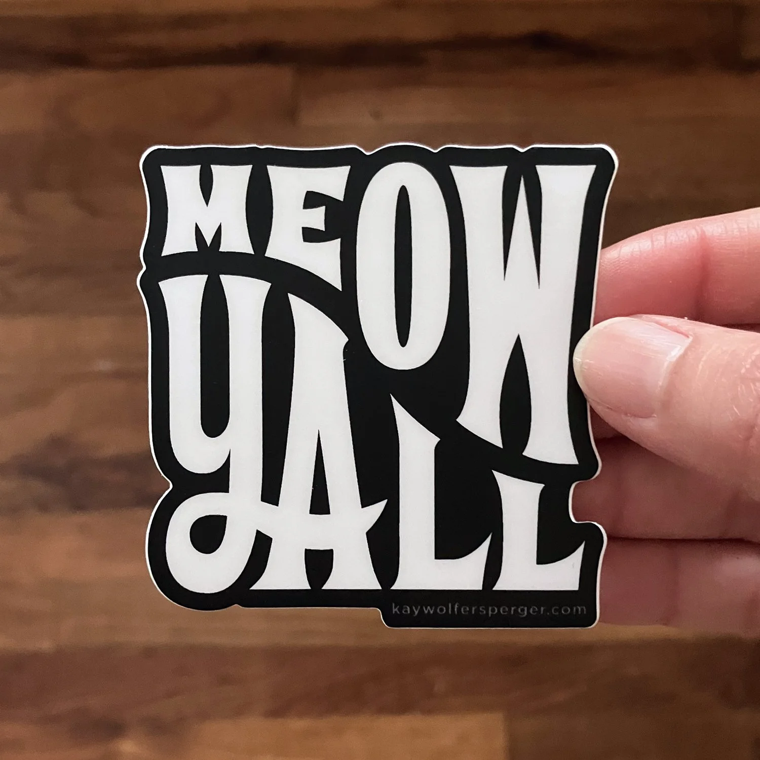 A hand is holding a black and white sticker that says "Meow Yourself" in stylized, bold lettering.