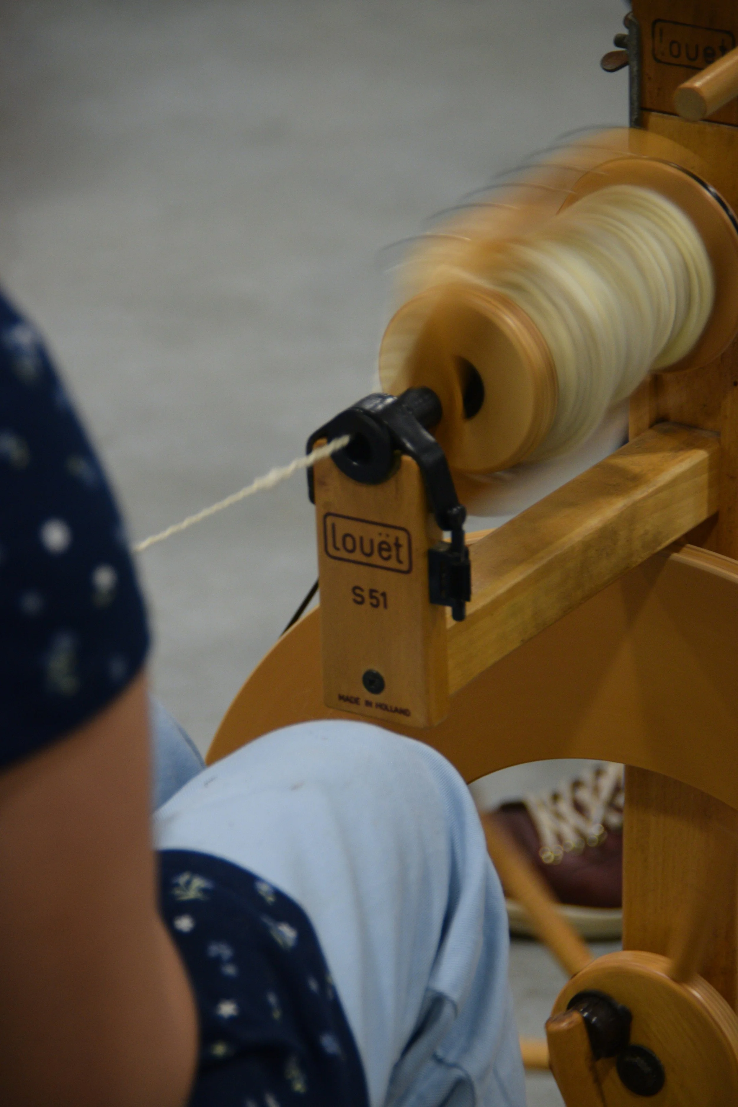 A person wearing a blue polka dot shirt and light blue shorts, sitting and operating a wooden spinner.