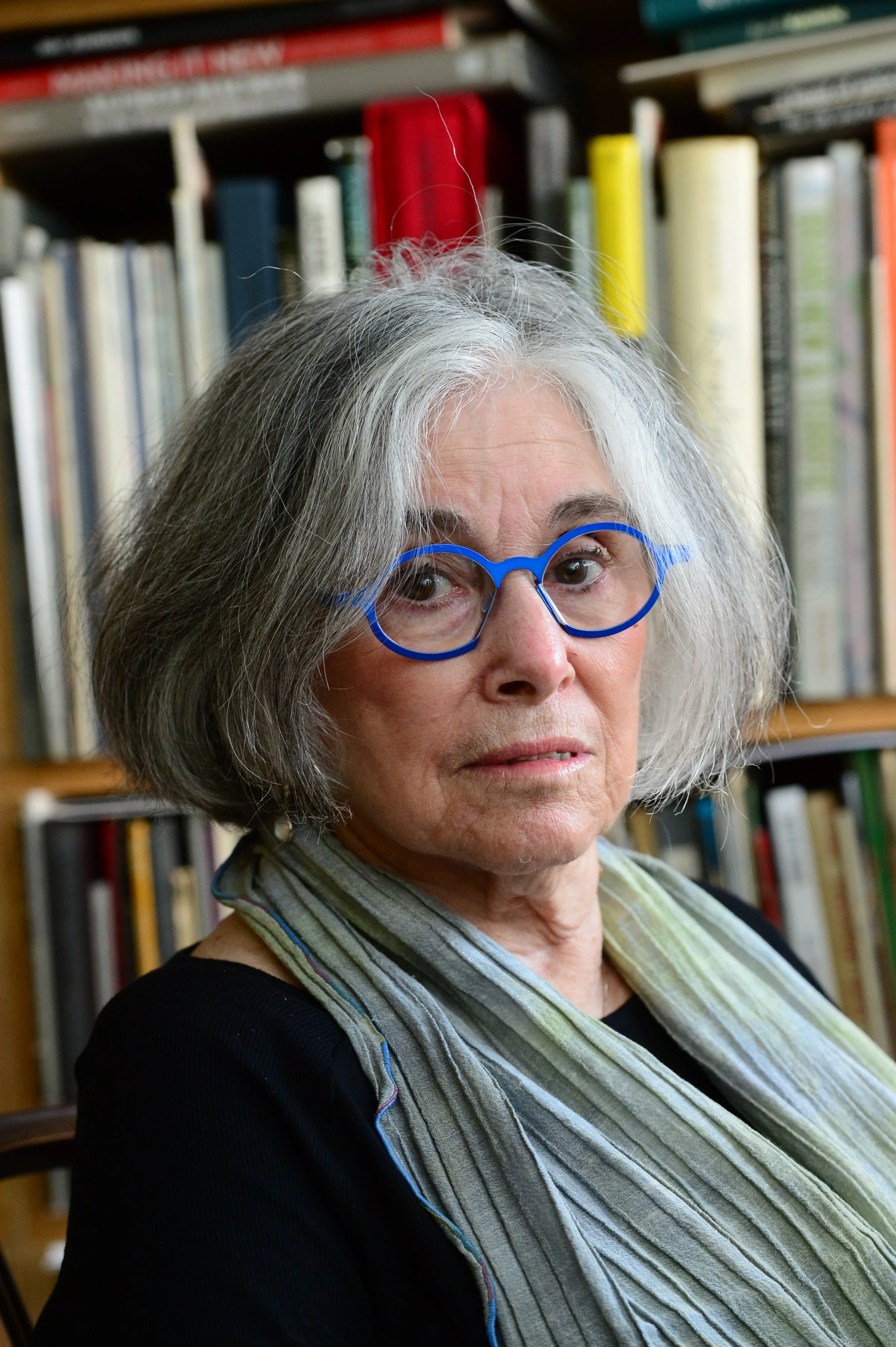 A portrait of Ruth E. Lehrer Fine, wearing distinctive blue glasses, seated in front of a bookshelf in her home in Philadelphia.