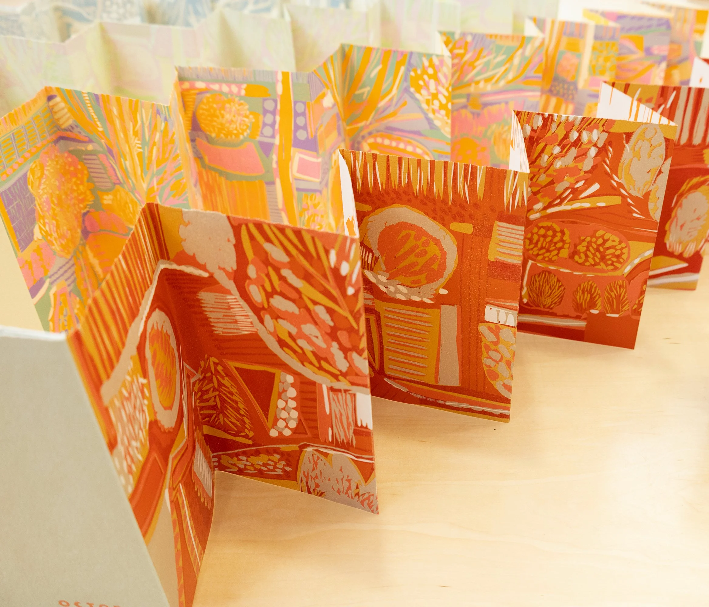 Colorful prints with orange, yellow, pink, and purple abstract patterns, representing the work of Ruth E. Fine, folded into a long accordion fold.