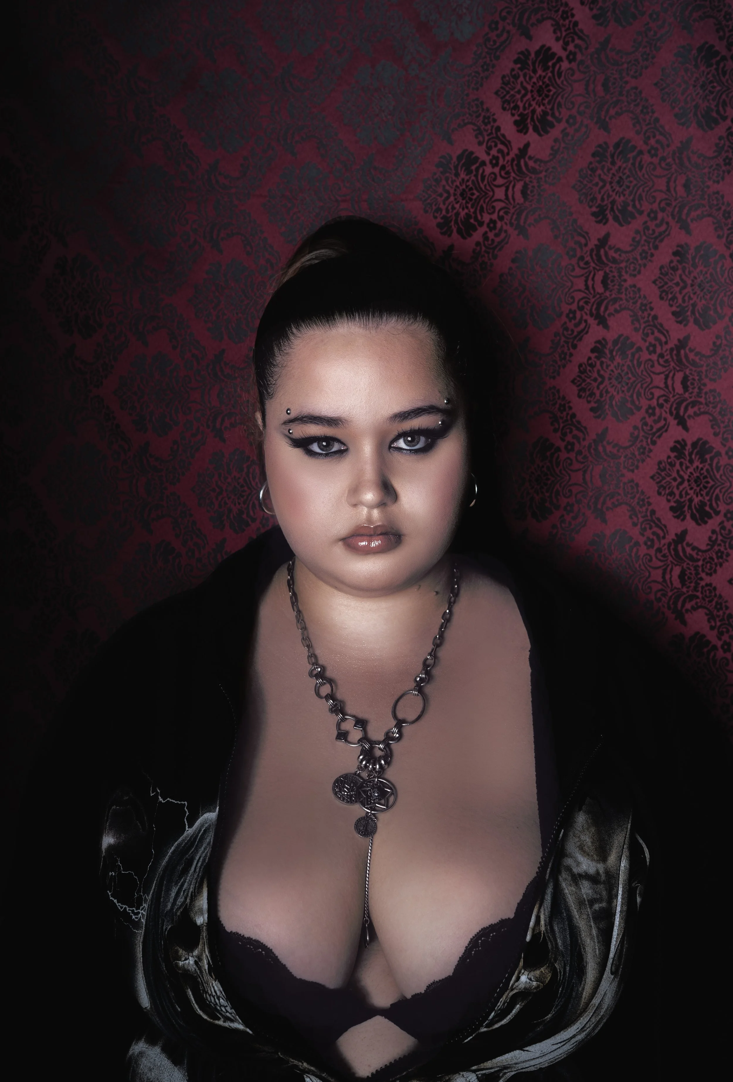 Portrait d'une femme portant un collier en métal et un haut en corset noir, avec un fond rouge avec motif décoratif.