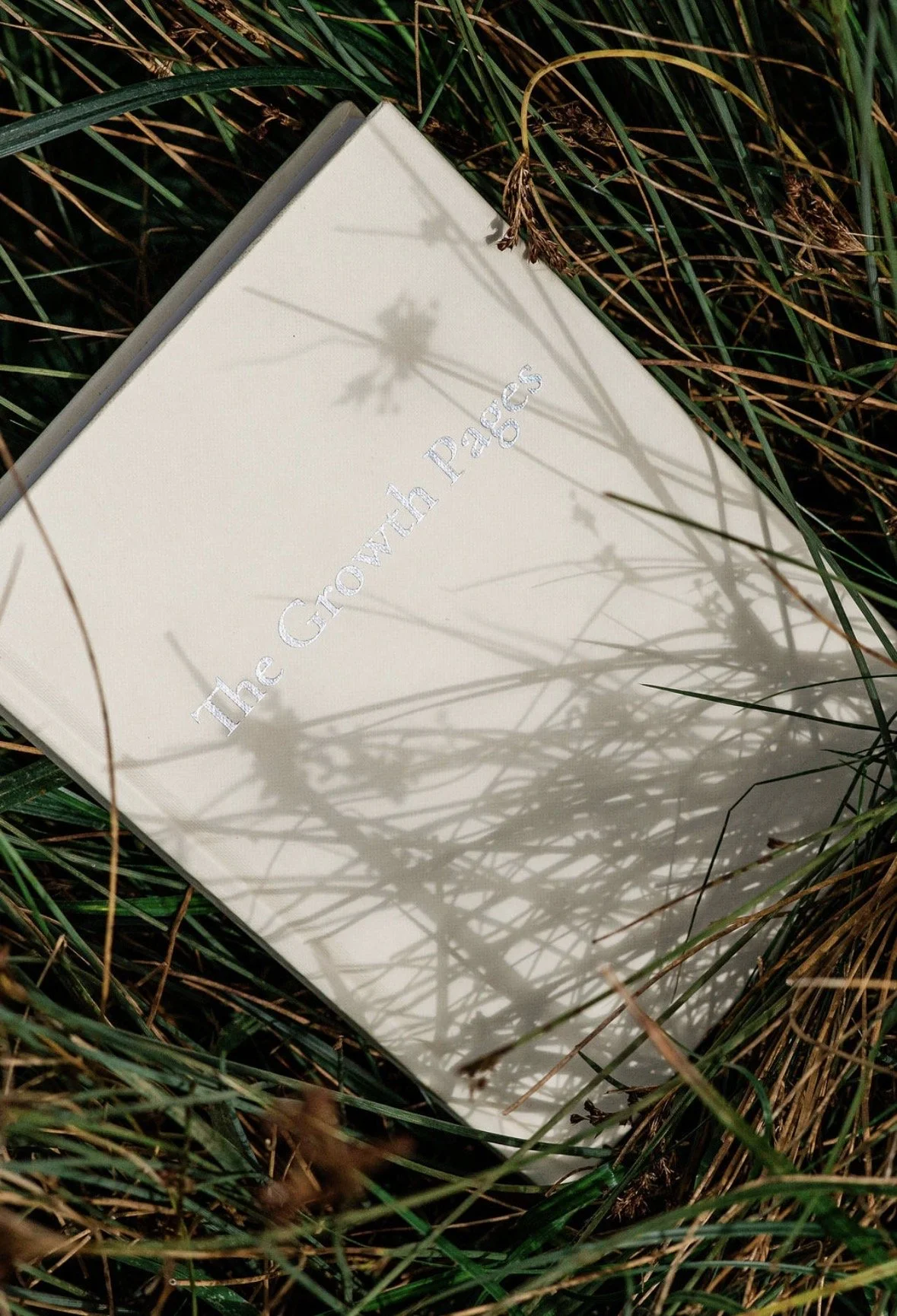 A book titled 'The Growth Pass' lying on grass, with shadow of plant stems cast on its cover.