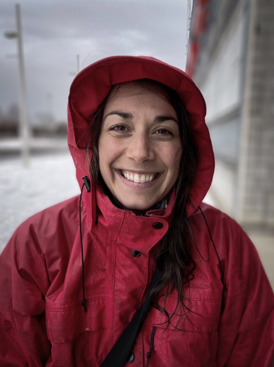 Une femme souriante portant une veste et un bonnet rouges, par temps de pluie.