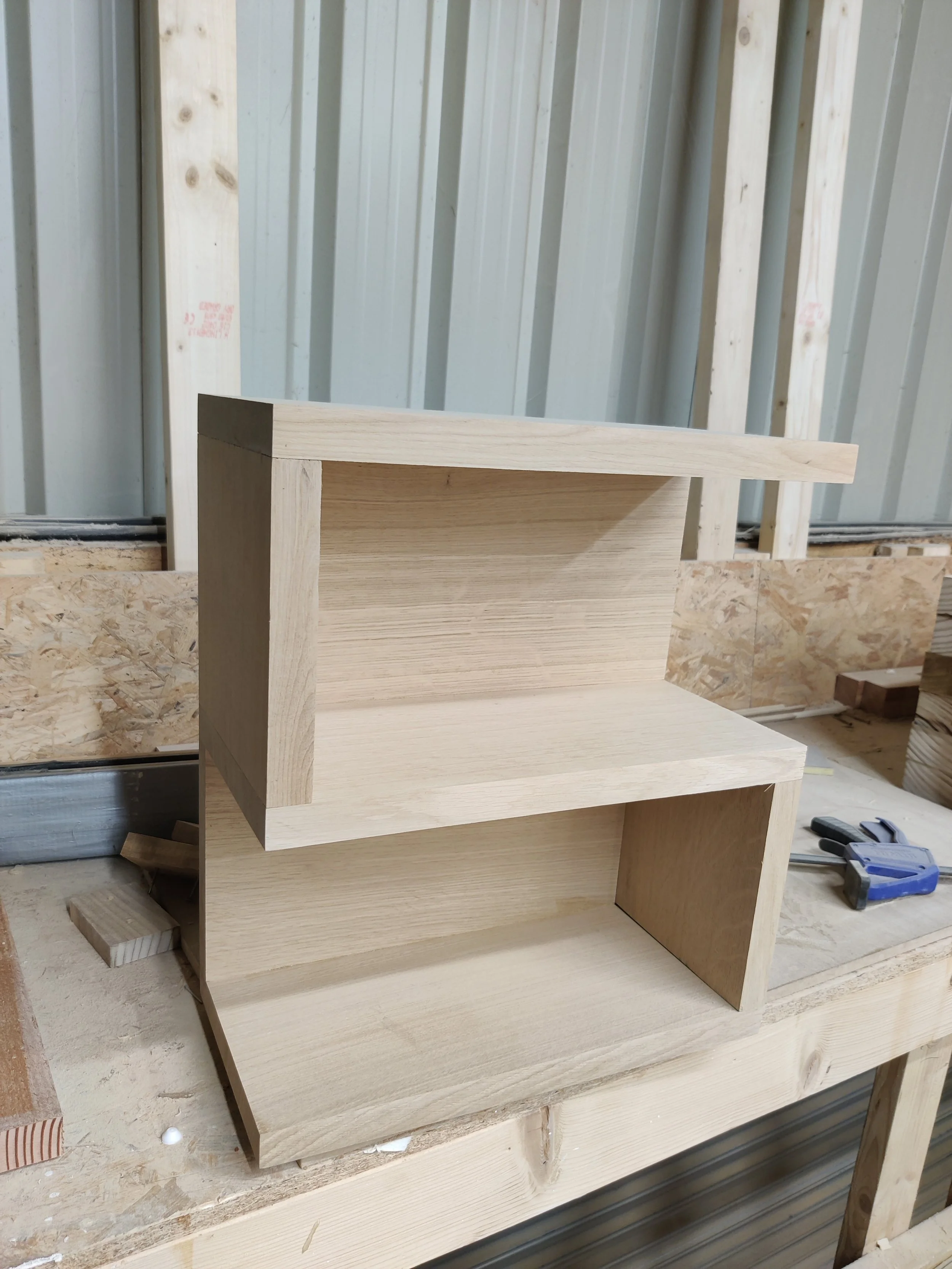 Wooden furniture piece under construction, placed on a workbench in a workshop with metal siding background.