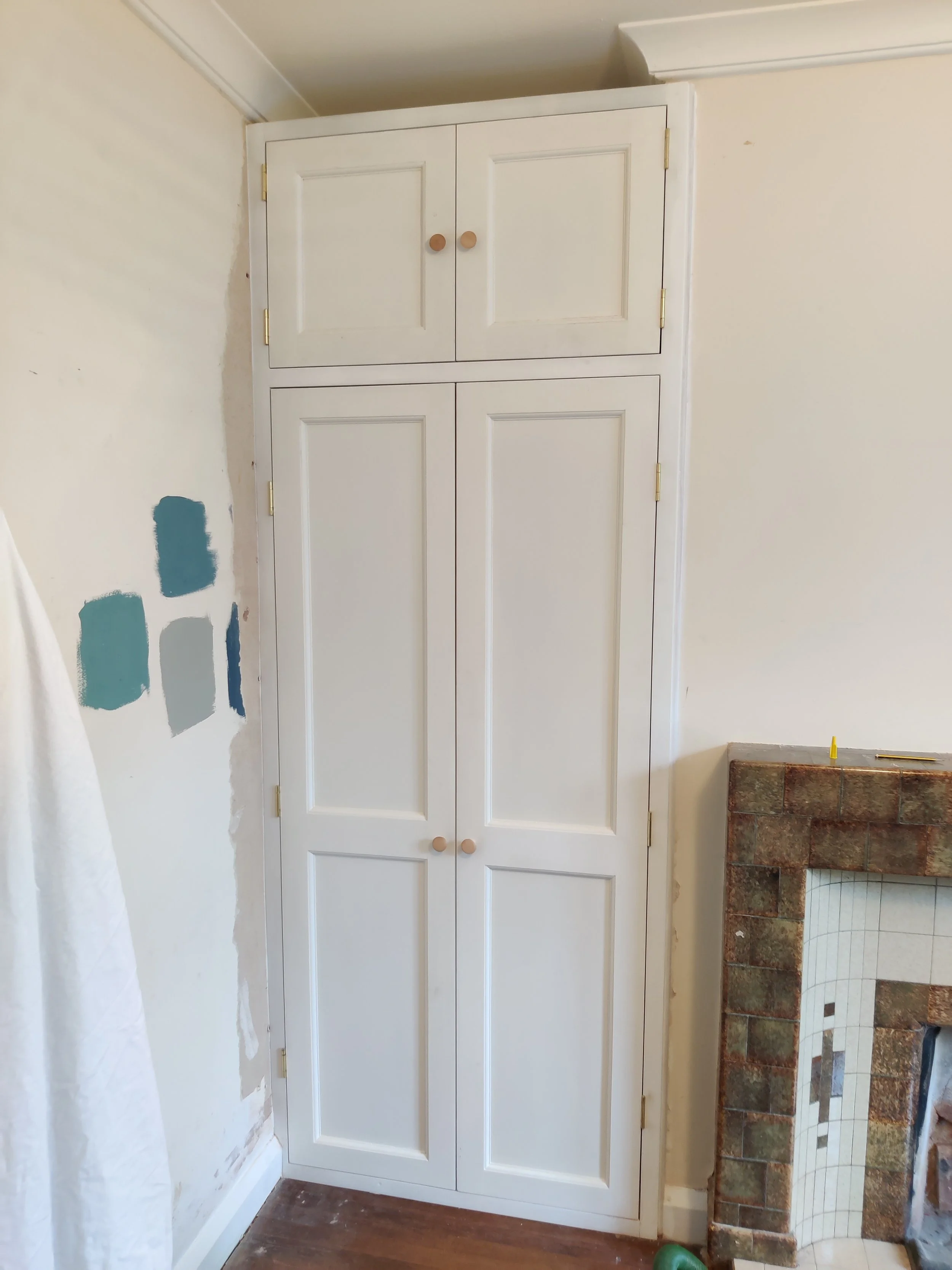 White wooden bespoke fitted cabinet with four doors and wooden knobs in a rooms alcove creating storage space.