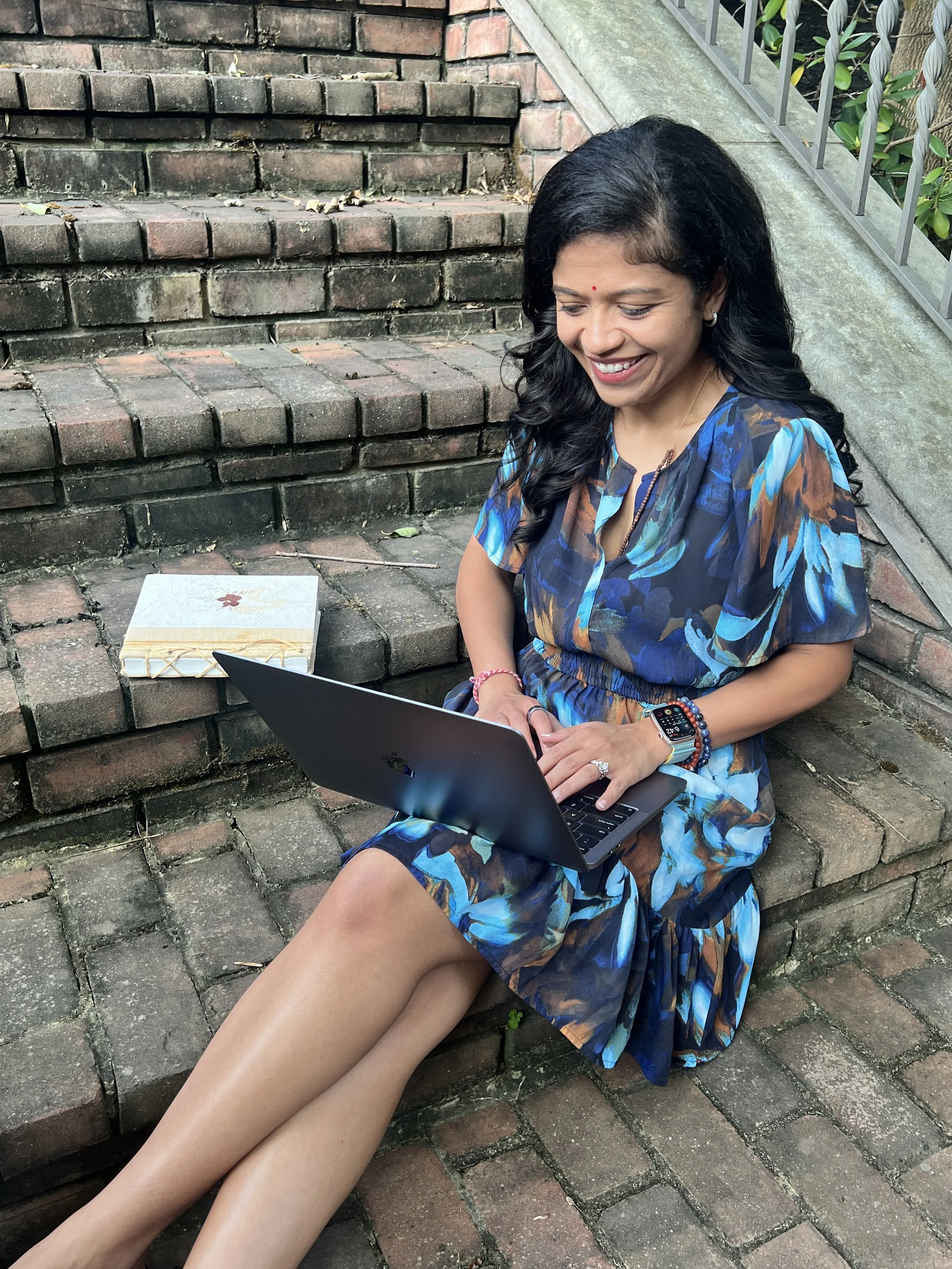 Nishi Jani Rajguru sitting outside with her laptop appearing to type on her laptop and communicate.