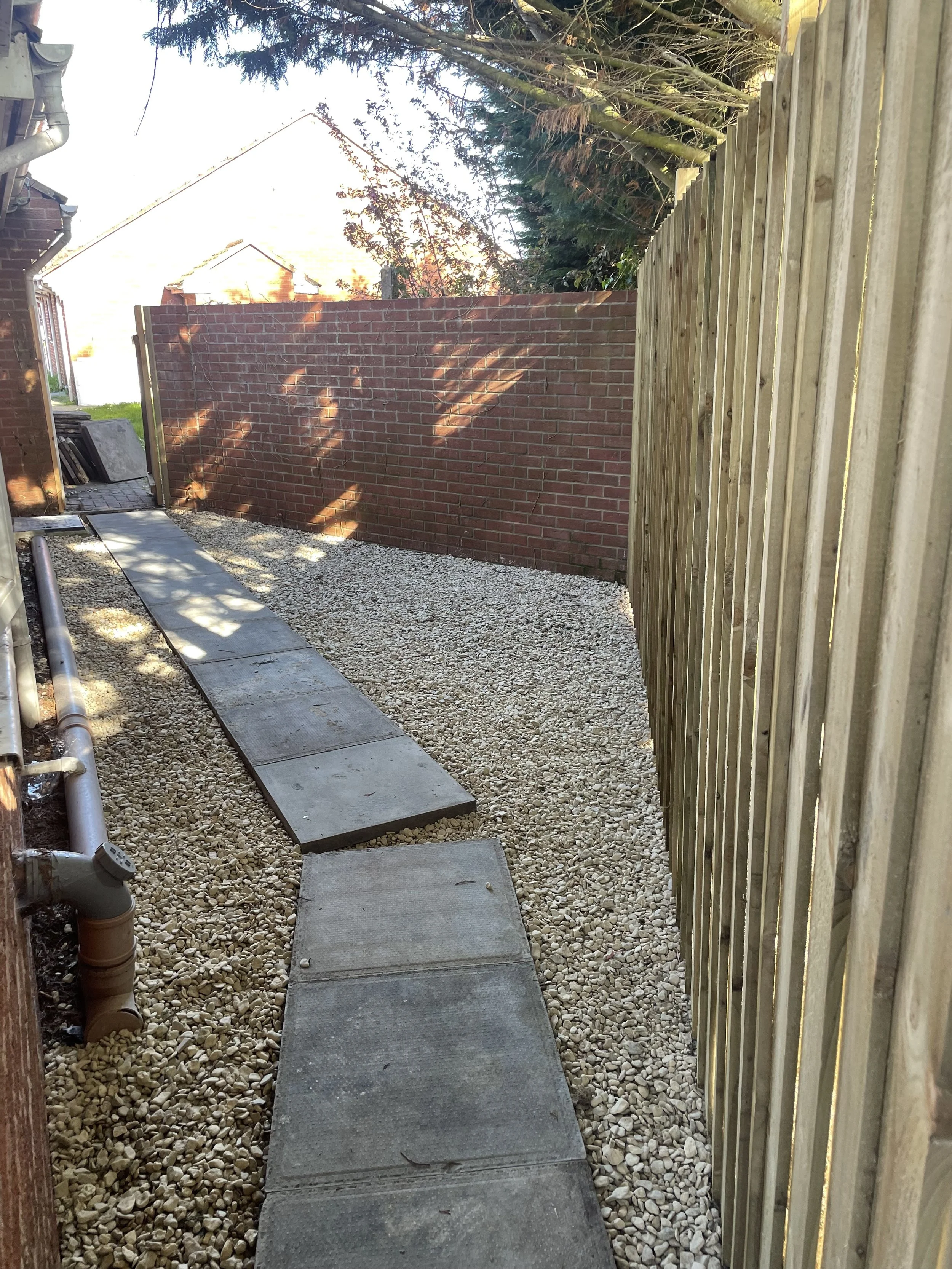 A narrow outdoor pathway with large concrete stepping stones on a gravel bed install by Britton Landscaping in Somerset