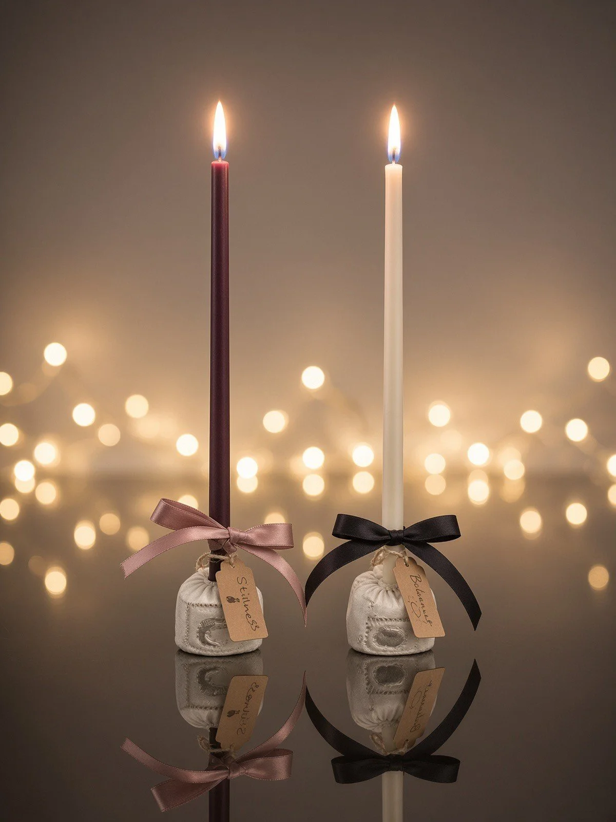 Two handmade taper candles, one deep plum and one cream, in small clay holders made in the Equinox session