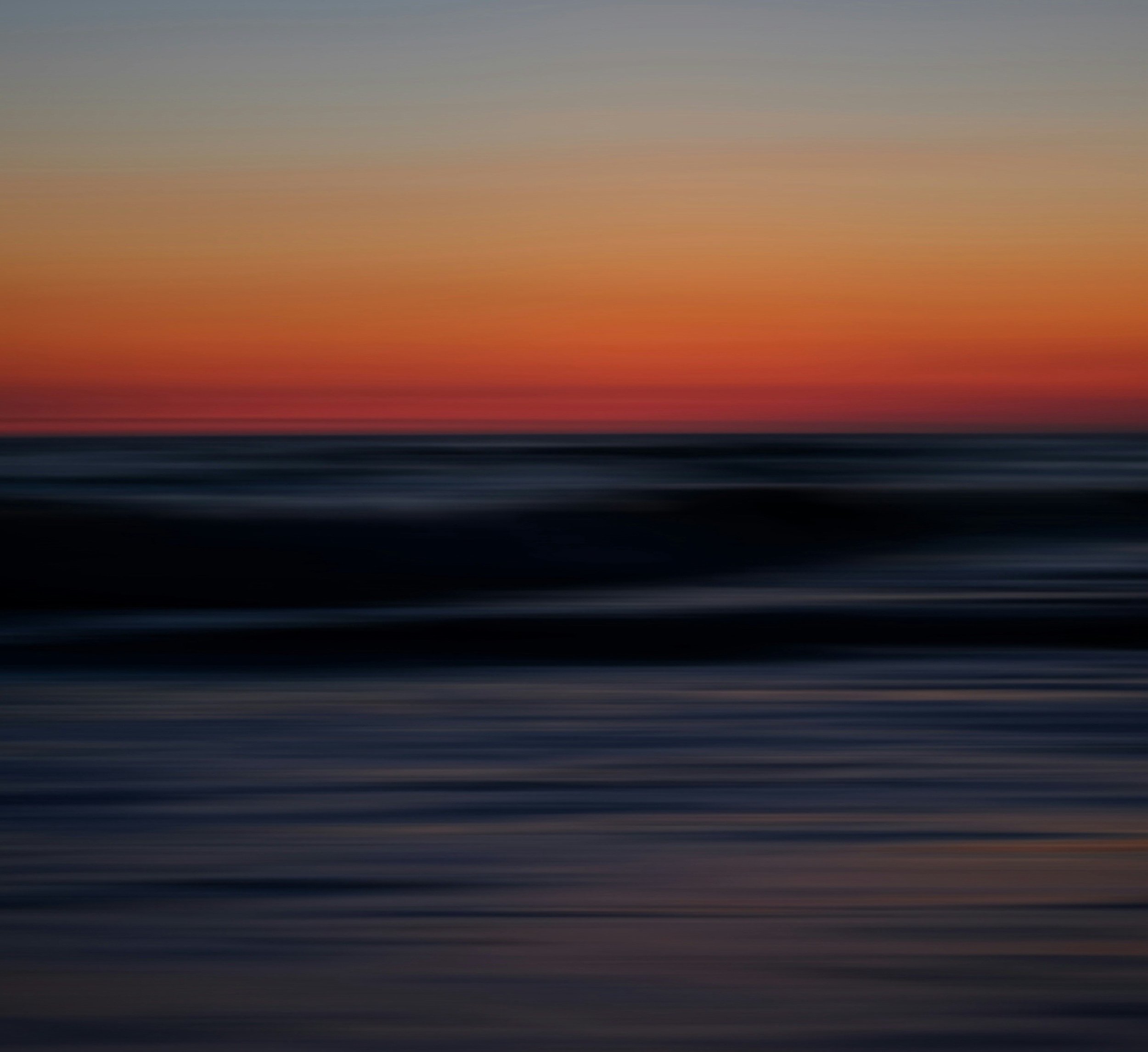 Blurred sunset over the sea, orange sky fading into dark water, equal measures of light and dark